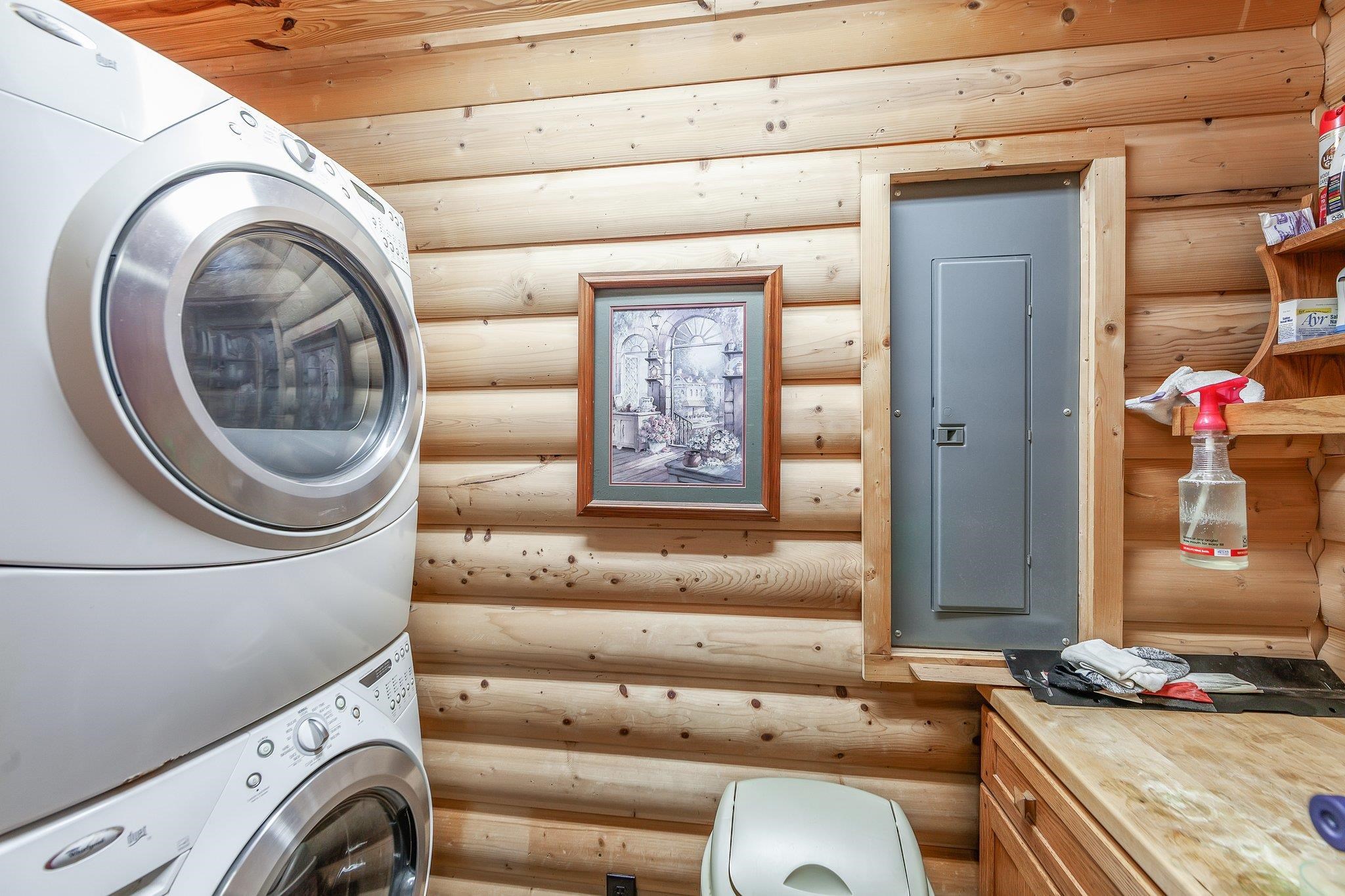 Washroom featuring stacked washing maching and dryer, rustic walls, electric panel, and wooden ceiling