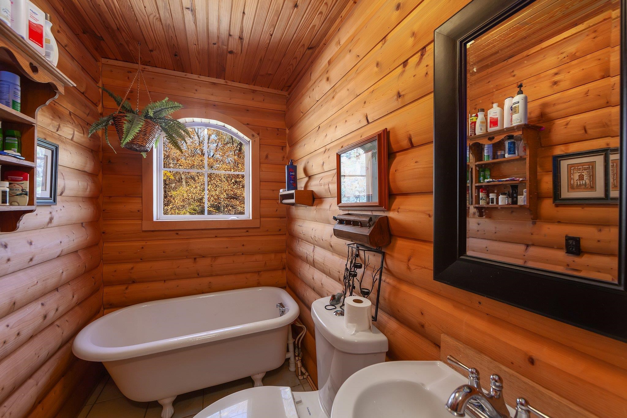 Bathroom with rustic walls, sink, a tub to relax in, toilet, and wood ceiling
