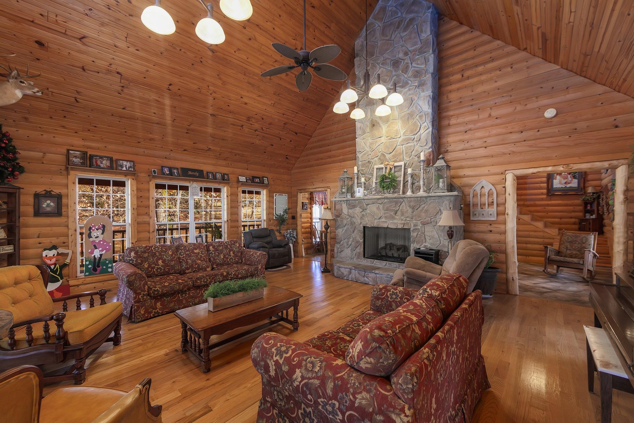 Living room featuring wood ceiling, ceiling fan, light hardwood / wood-style flooring, high vaulted ceiling, and a stone fireplace