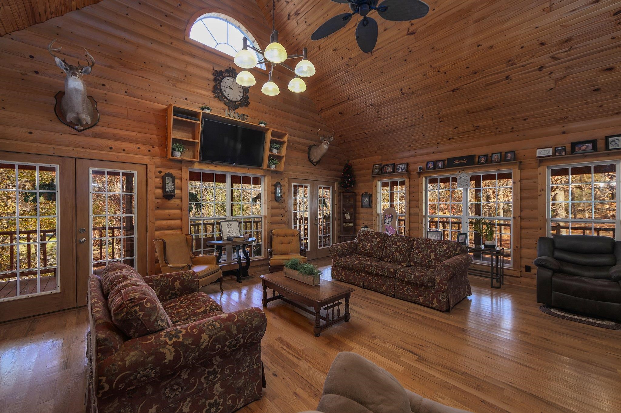 Living room with wood walls, hardwood / wood-style floors, high vaulted ceiling, and ceiling fan with notable chandelier