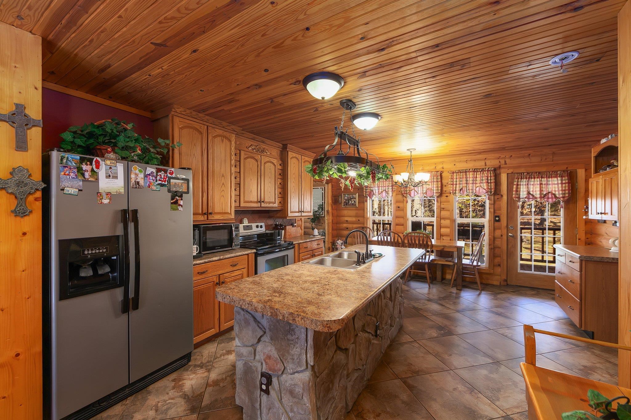 Kitchen with appliances with stainless steel finishes, wood ceiling, sink, hanging light fixtures, and an island with sink