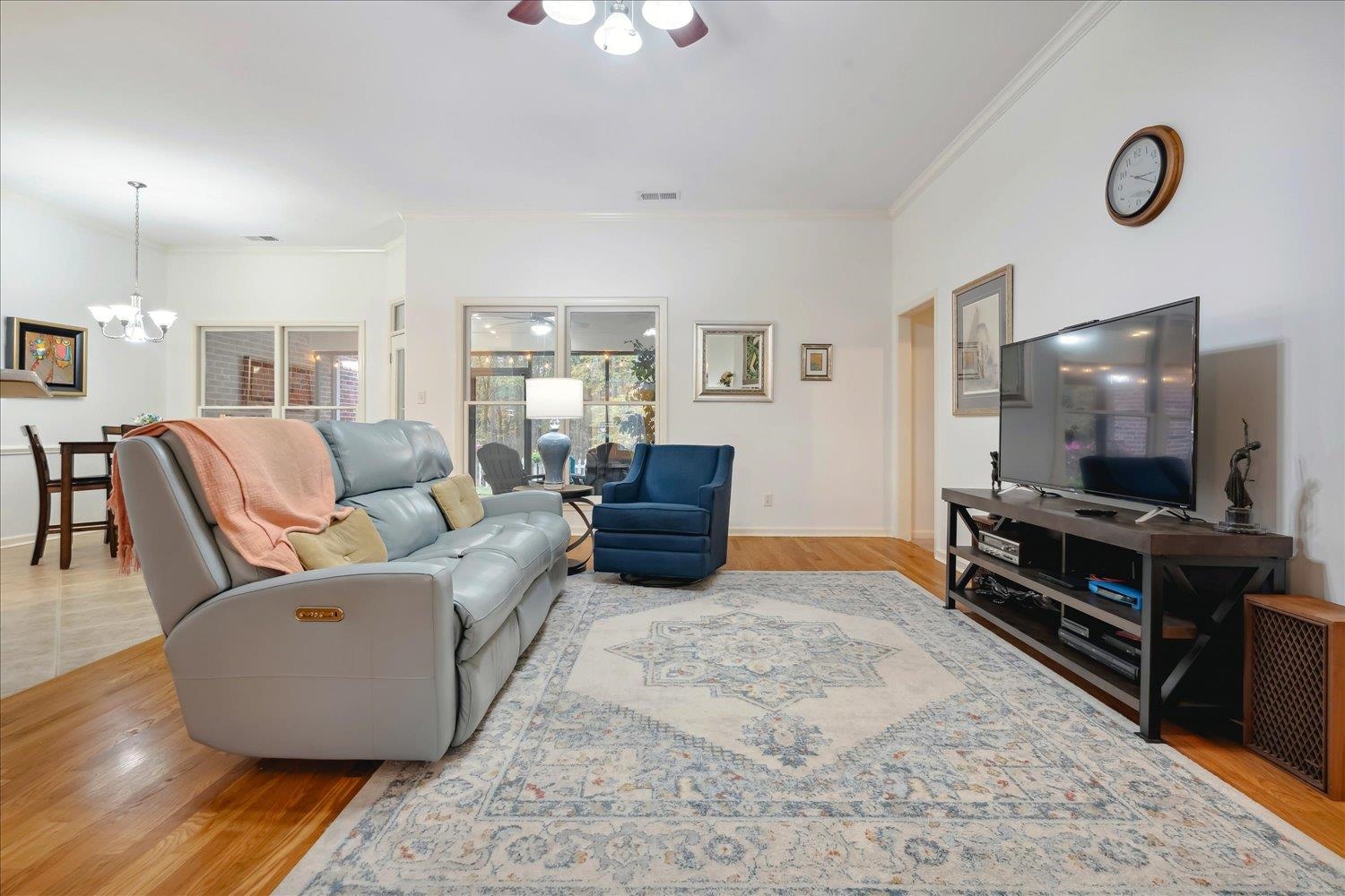 Great roomwith ceiling fan with notable chandelier, light wood-type flooring, and crown molding