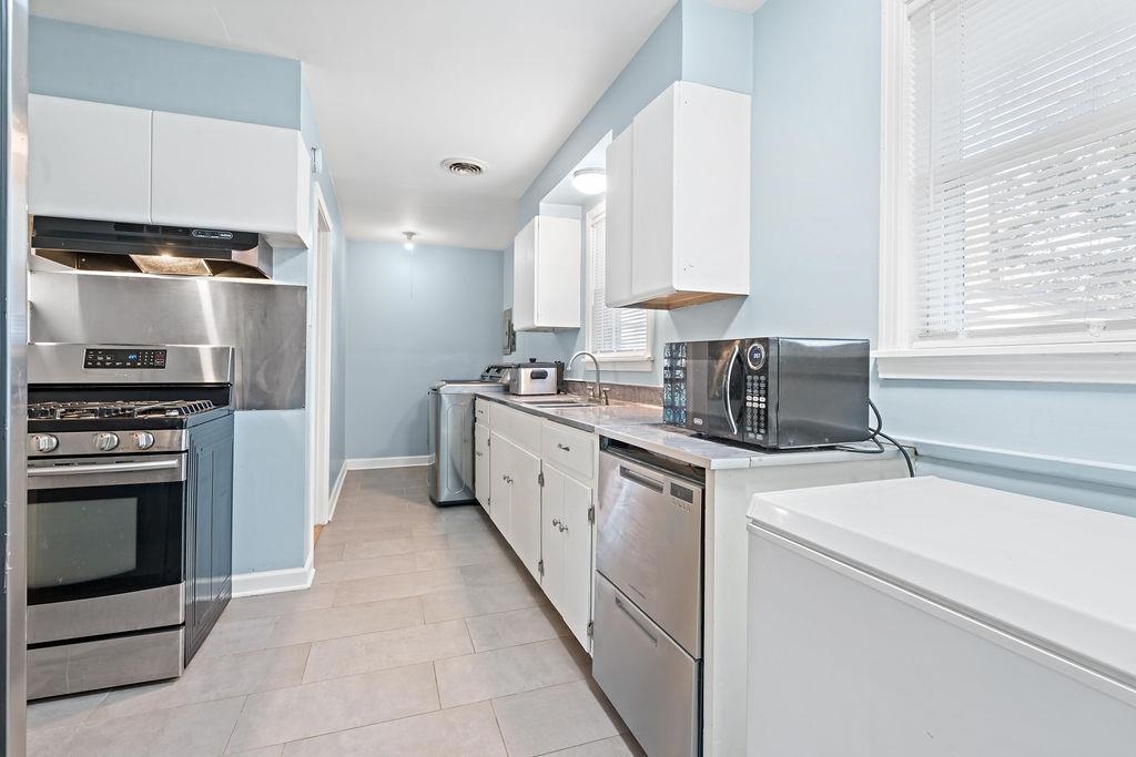 Kitchen featuring white cabinetry, sink, stainless steel appliances, ventilation hood, and washer / clothes dryer