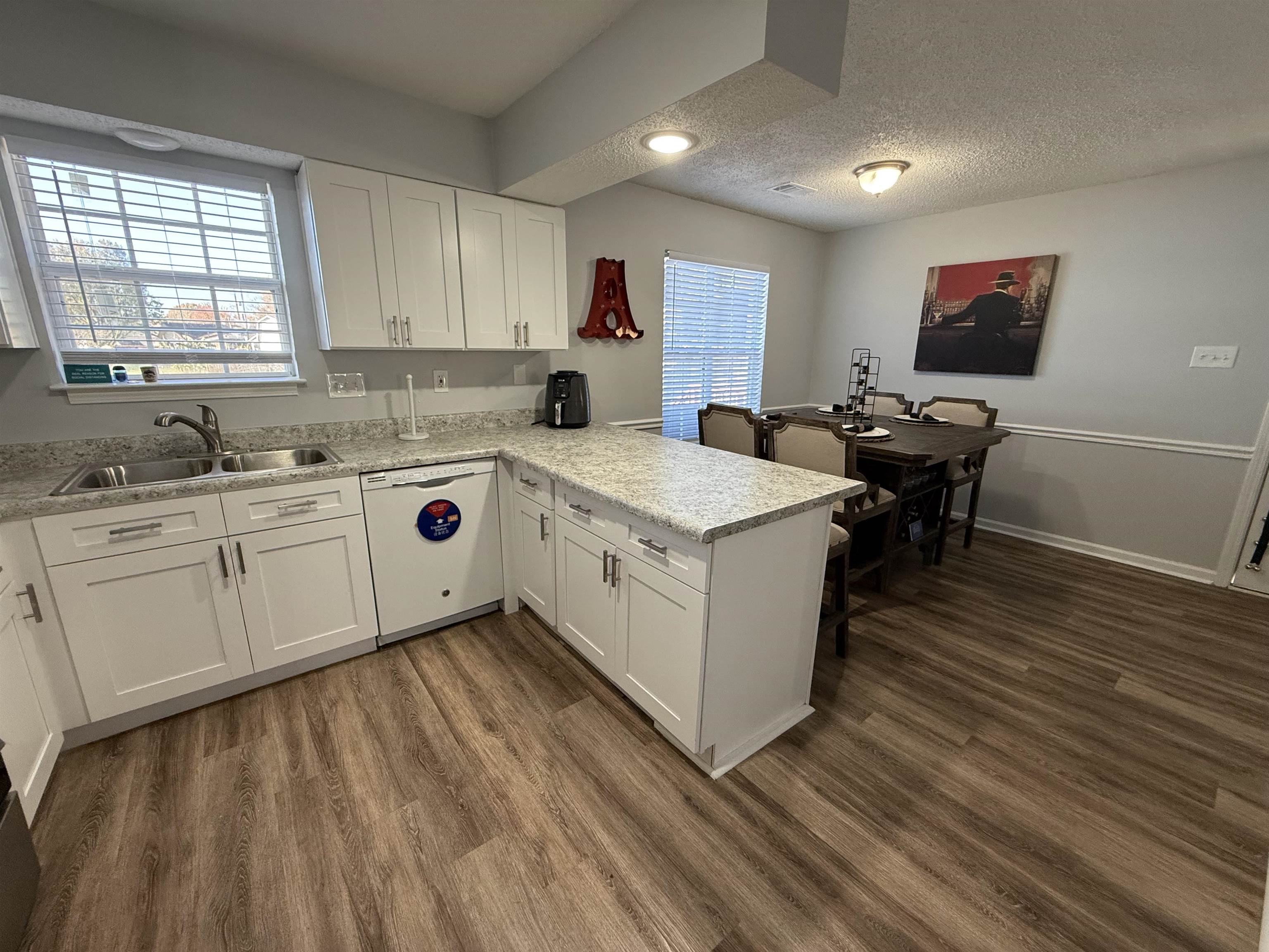 Kitchen featuring kitchen peninsula, sink, dishwasher, white cabinets, and dark hardwood / wood-style floors