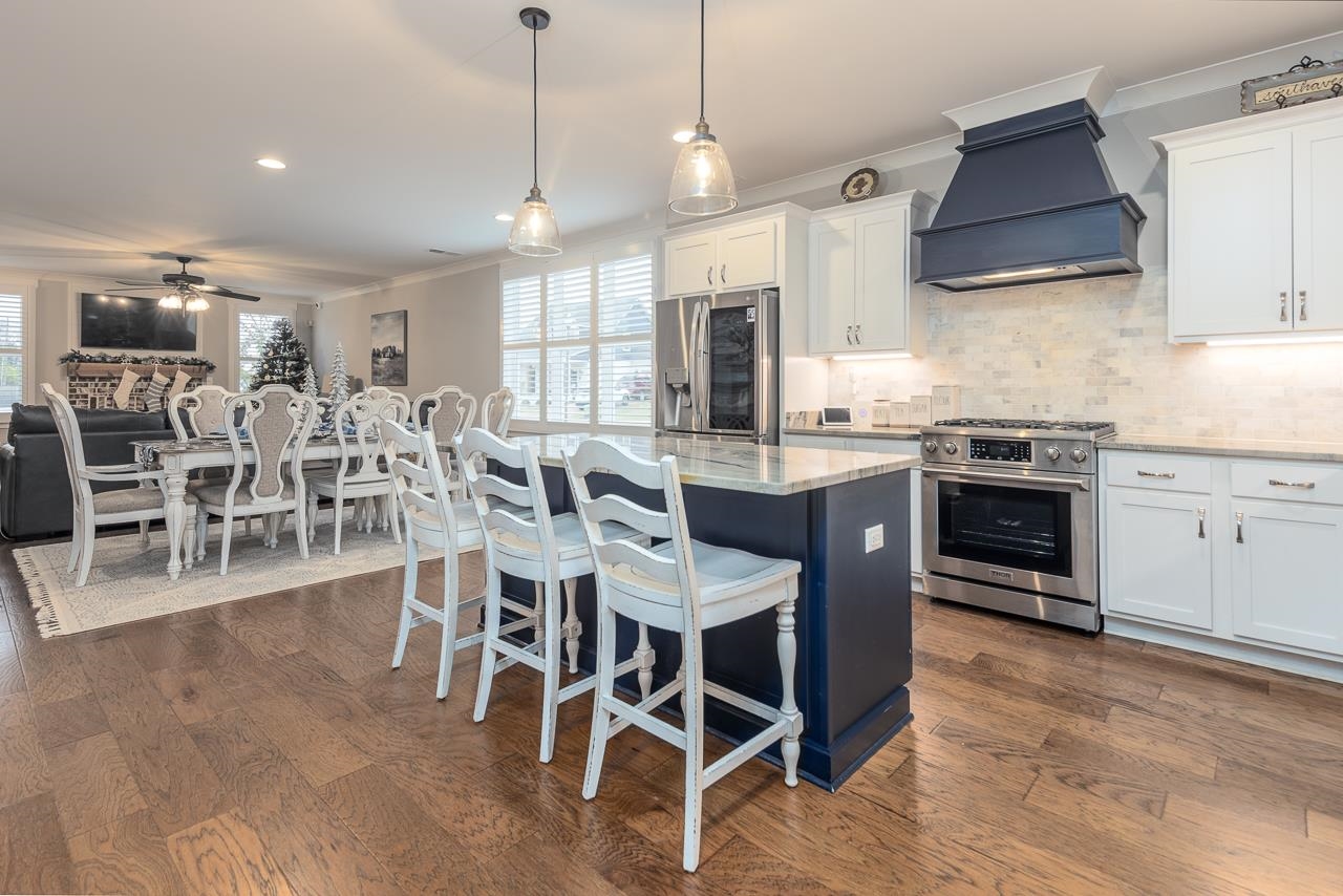 Kitchen featuring appliances with stainless steel finishes, premium range hood, white cabinetry, and plenty of natural light