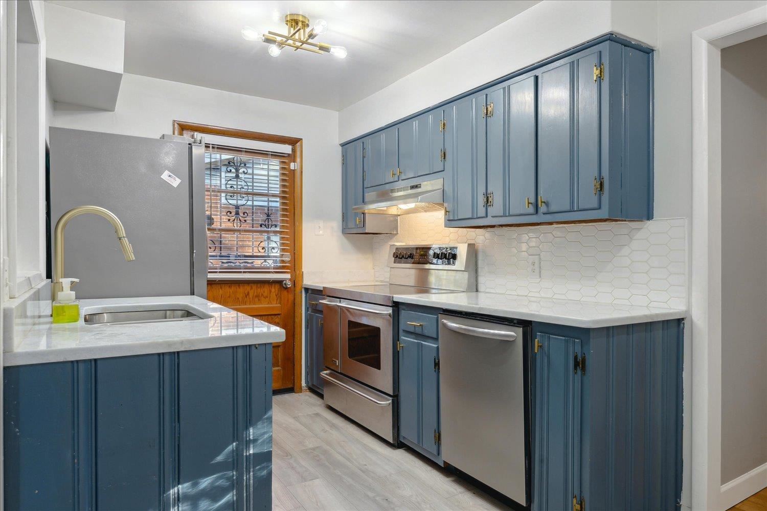 Kitchen featuring sink, stainless steel appliances, blue cabinets, light hardwood / wood-style floors, and decorative backsplash
