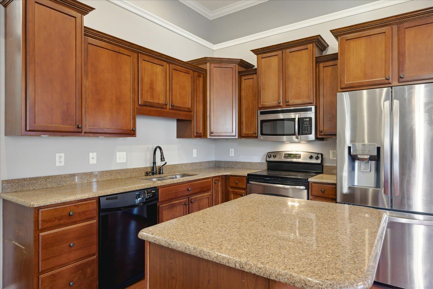 Kitchen featuring sink, ornamental molding, appliances with stainless steel finishes, a kitchen island, and light stone counters