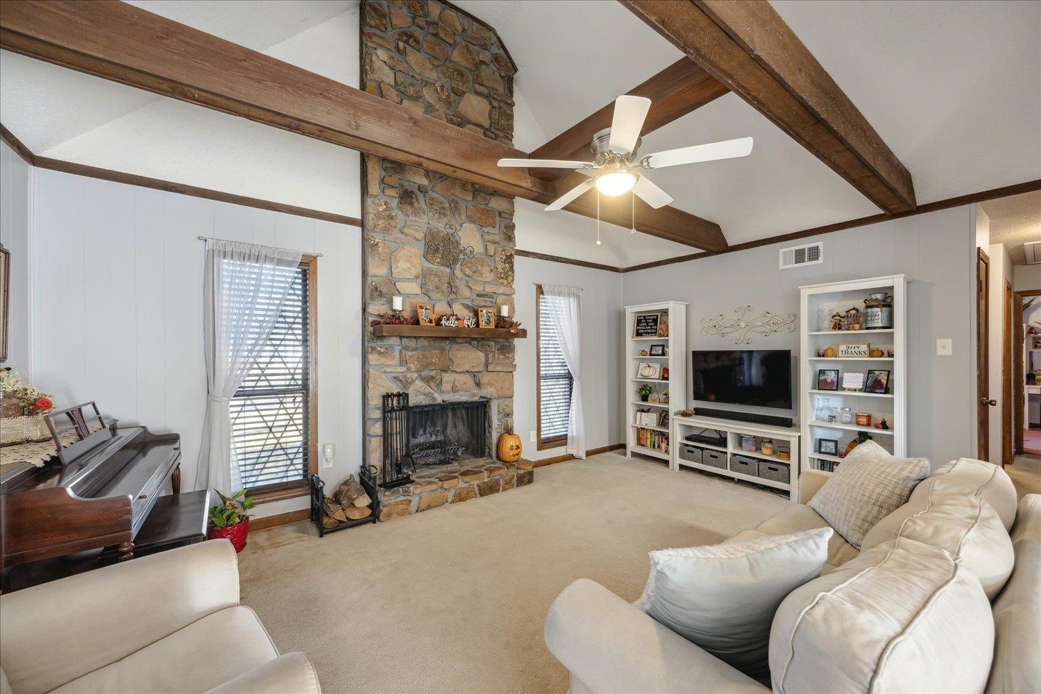 Living room with a fireplace, beam ceiling, light colored carpet, and a wealth of natural light