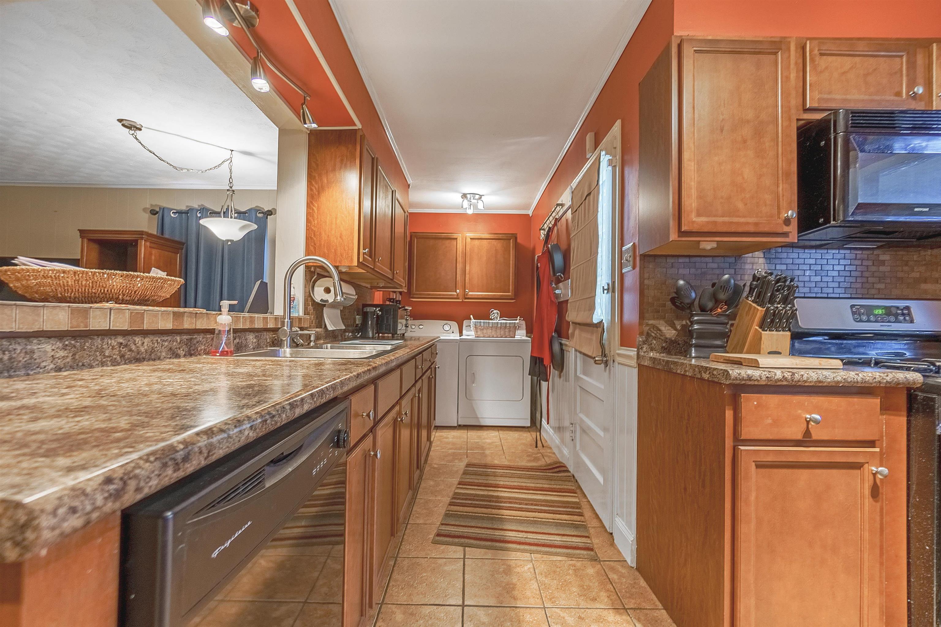 Kitchen featuring backsplash, sink, washer and dryer, light tile patterned floors, and black appliances