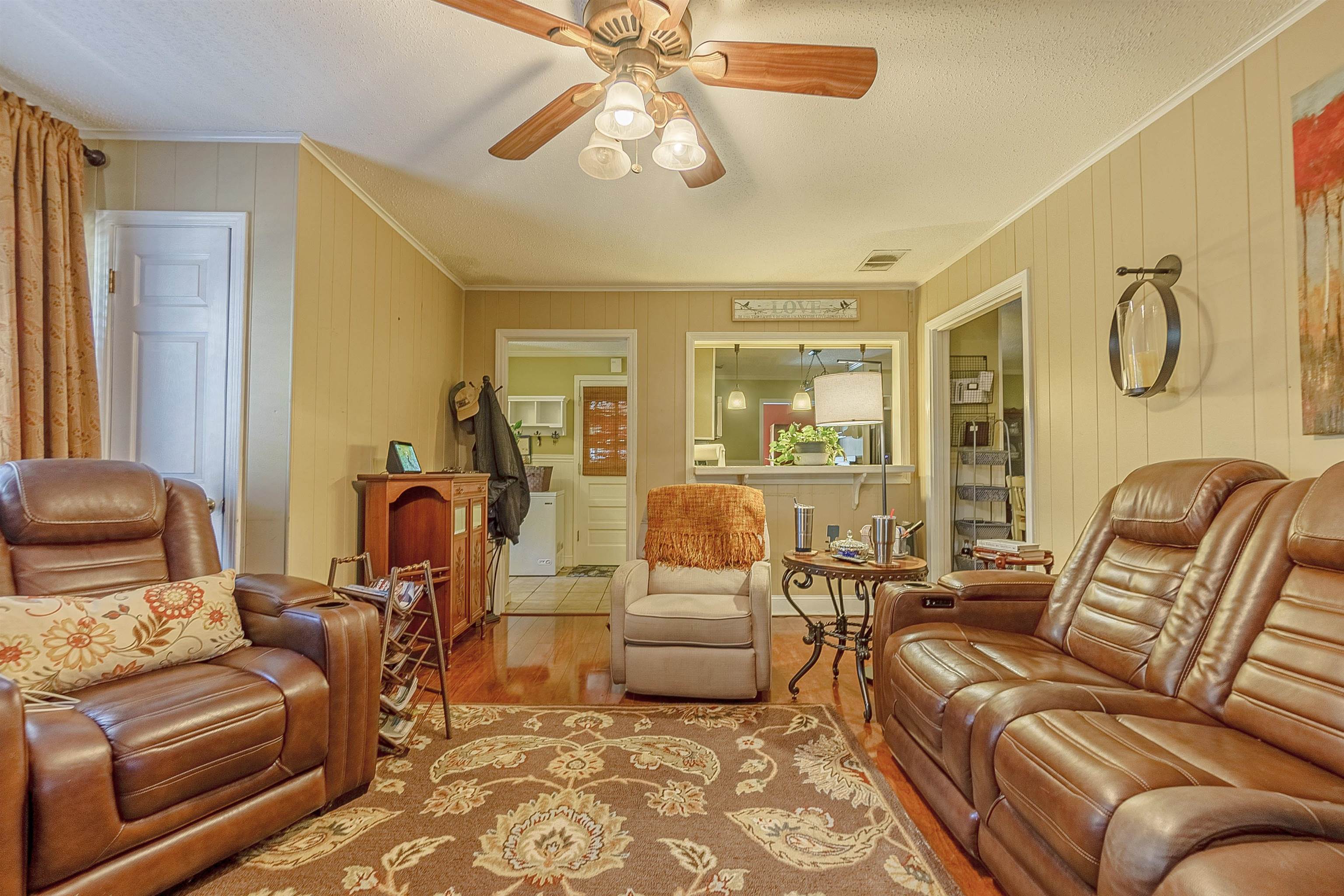 Living room featuring ceiling fan, crown molding, wood-type flooring, and wooden walls