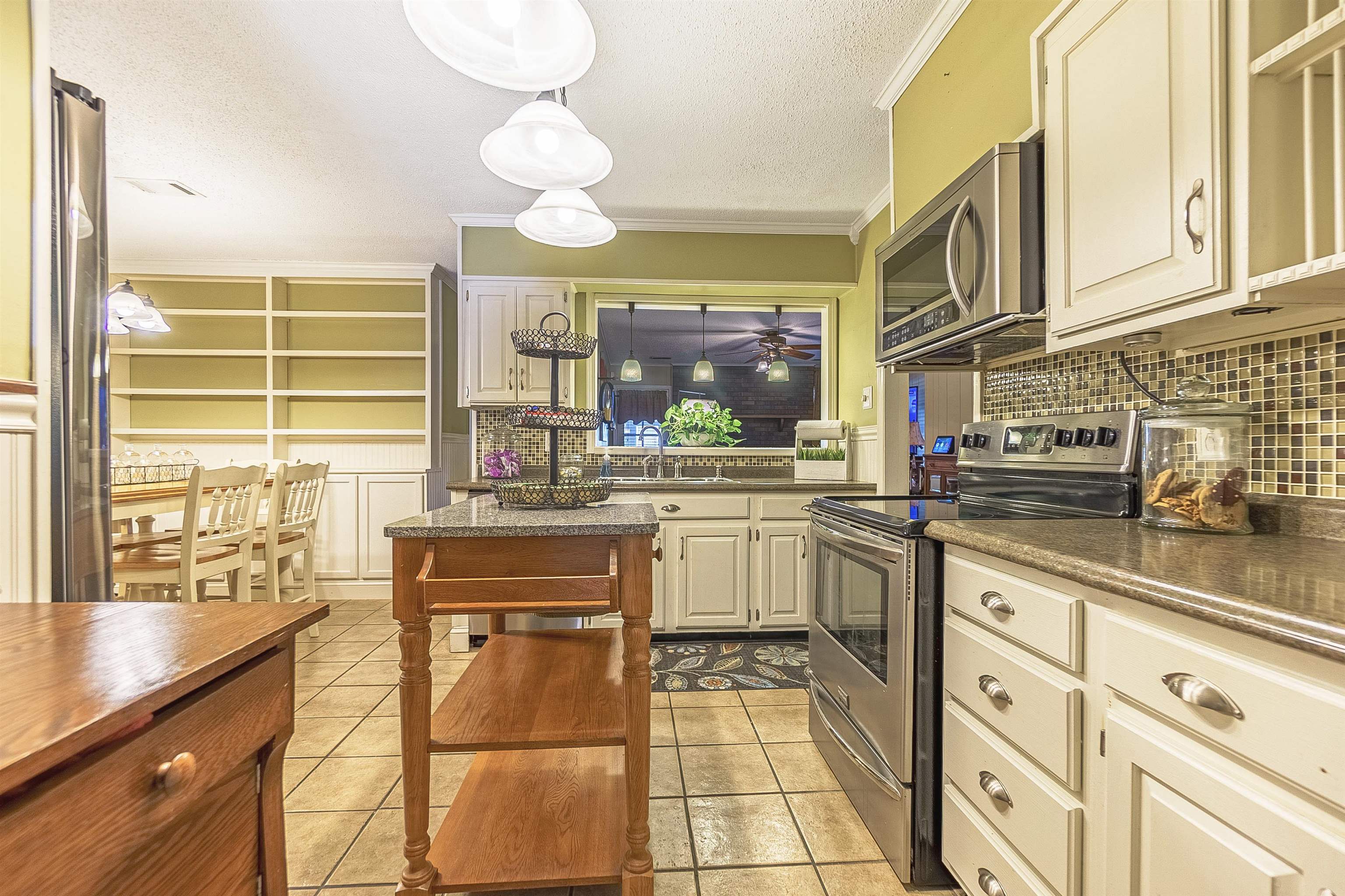 Kitchen featuring appliances with stainless steel finishes, tasteful backsplash, crown molding, cream cabinetry, and hanging light fixtures