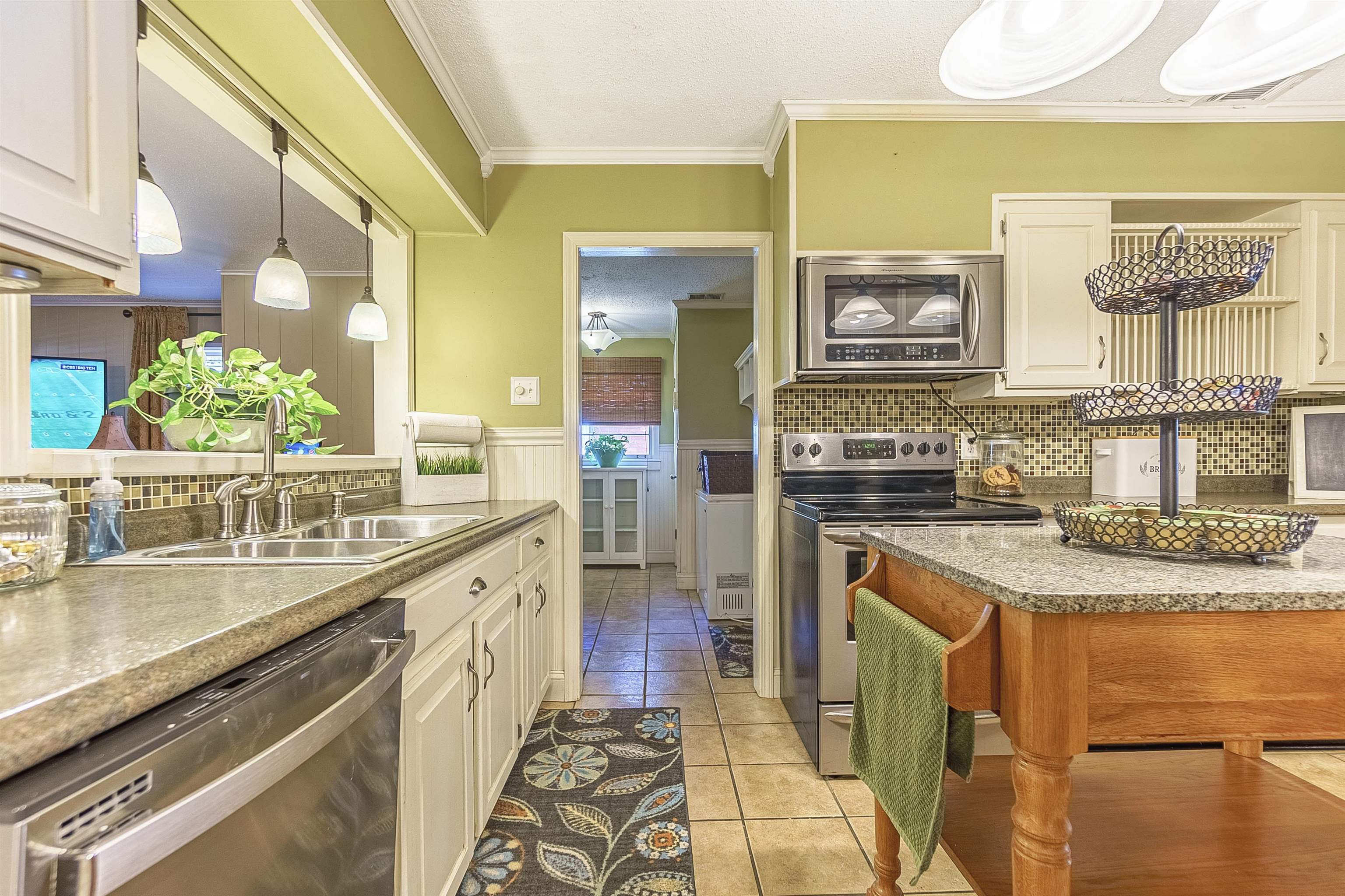 Kitchen featuring sink, crown molding, pendant lighting, light tile patterned floors, and appliances with stainless steel finishes