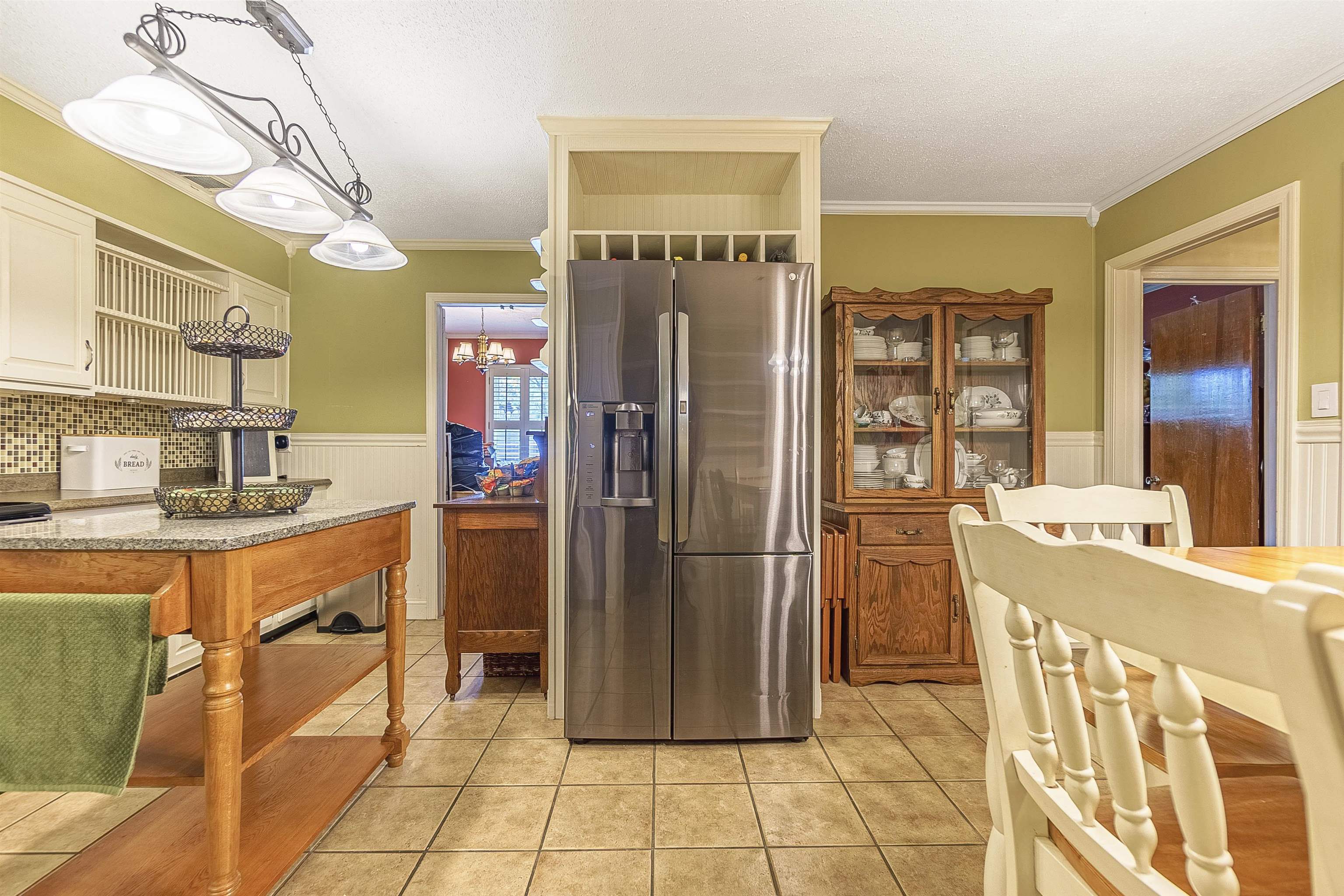 Kitchen with stainless steel fridge, light stone countertops, ornamental molding, decorative light fixtures, and light tile patterned flooring
