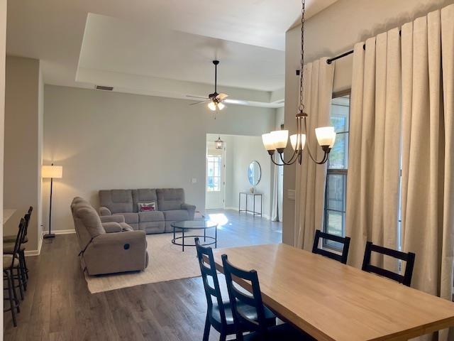 Dining space with a raised ceiling, dark hardwood / wood-style flooring, and ceiling fan with notable chandelier