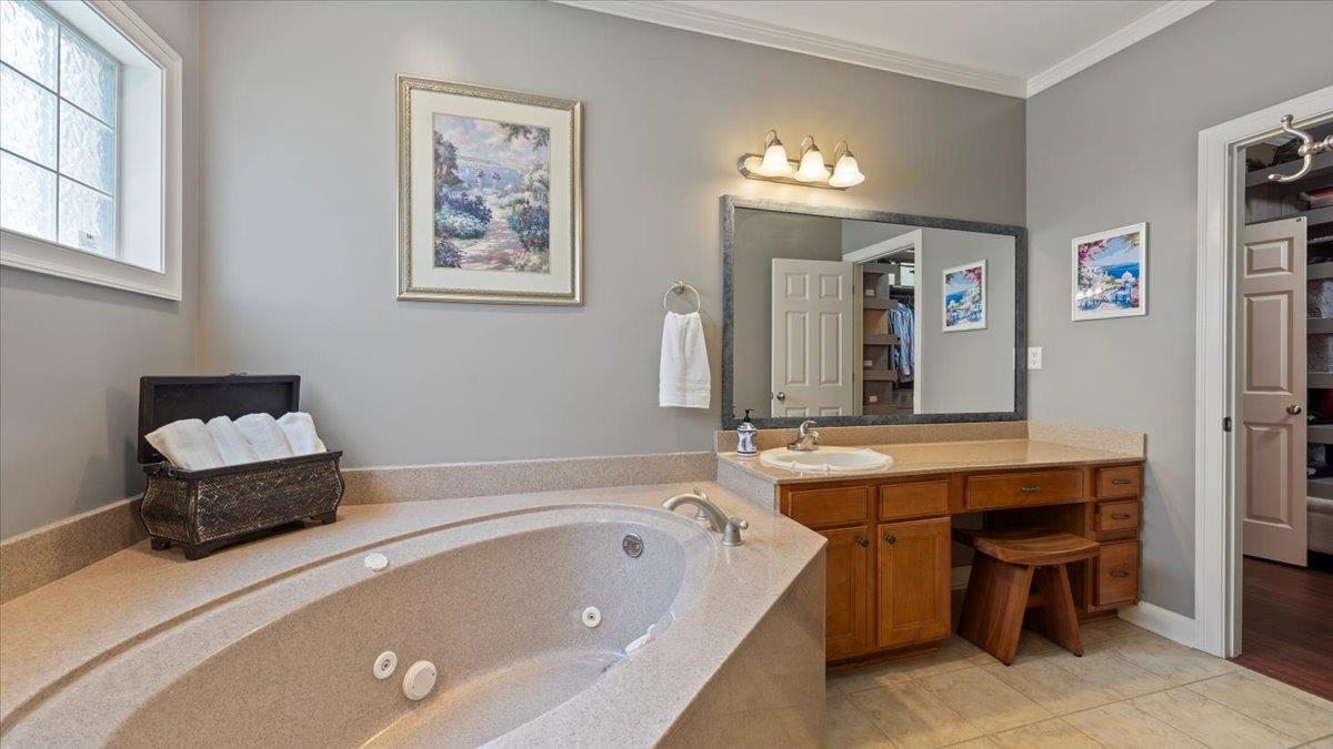 Bathroom featuring ornamental molding, vanity, tile patterned floors, and a tub to relax in