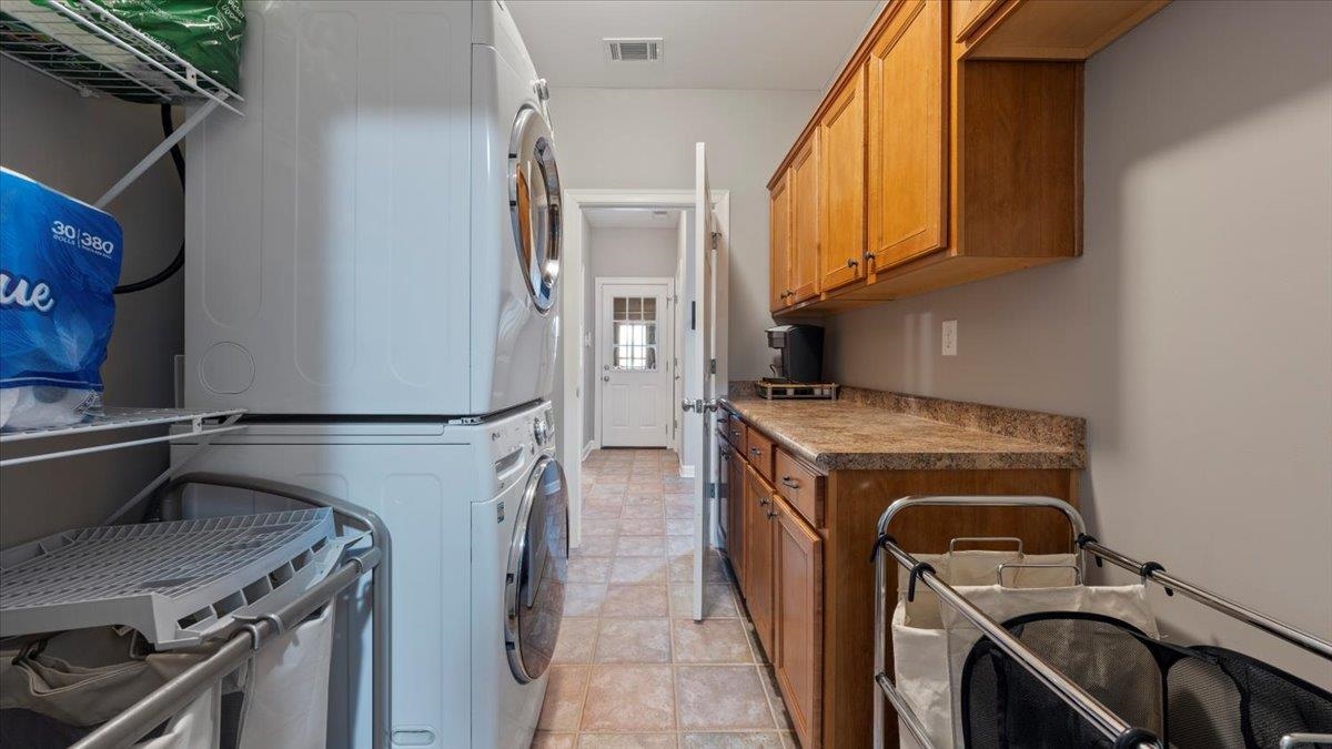 Laundry area featuring light tile patterned flooring, stacked washer and clothes dryer, and cabinets