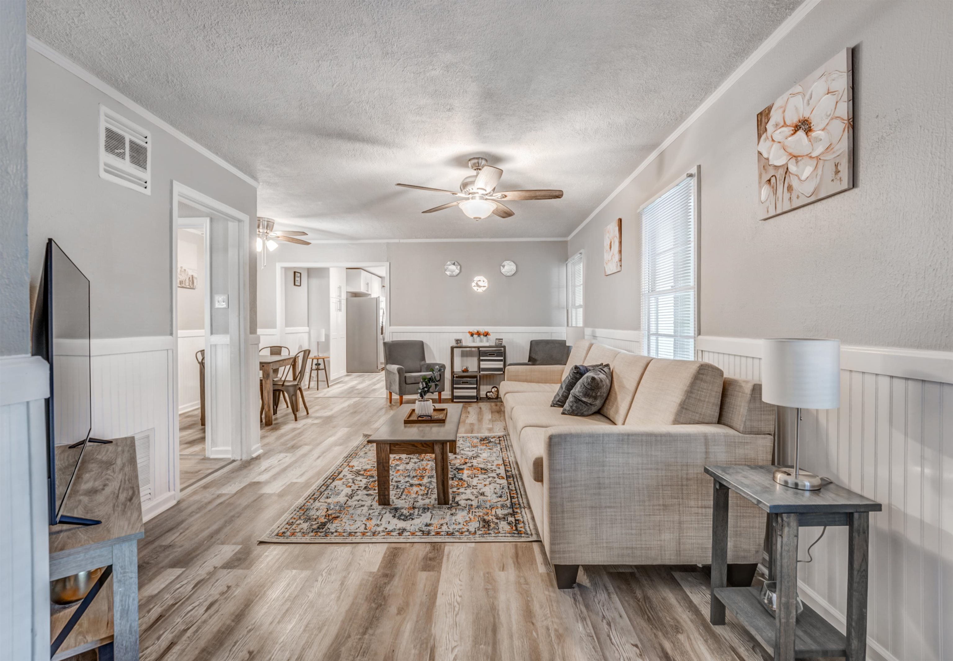 Living room with ceiling fan, ornamental molding, a textured ceiling, and light wood-type flooring
