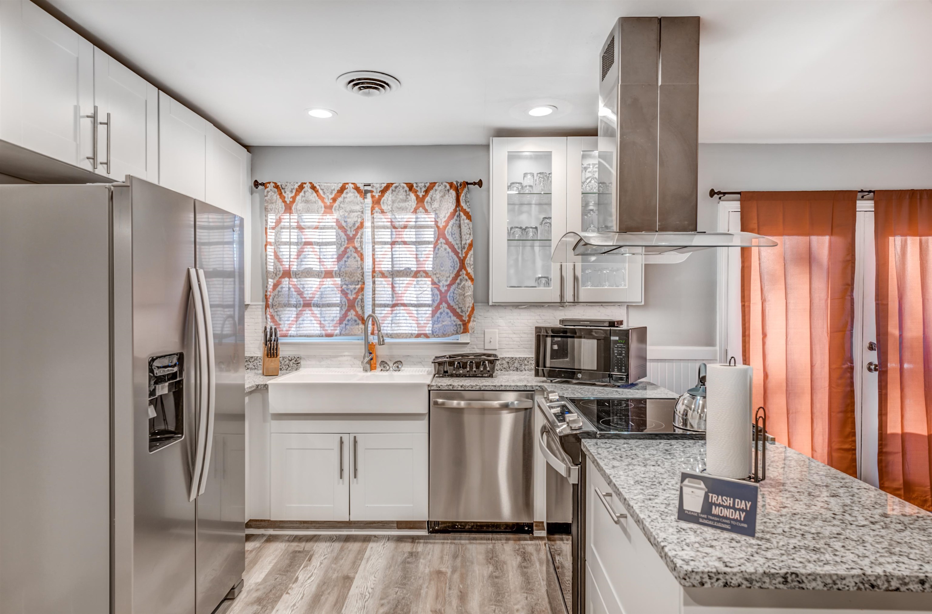 Kitchen with white cabinets, appliances with stainless steel finishes, light wood-type flooring, and island range hood