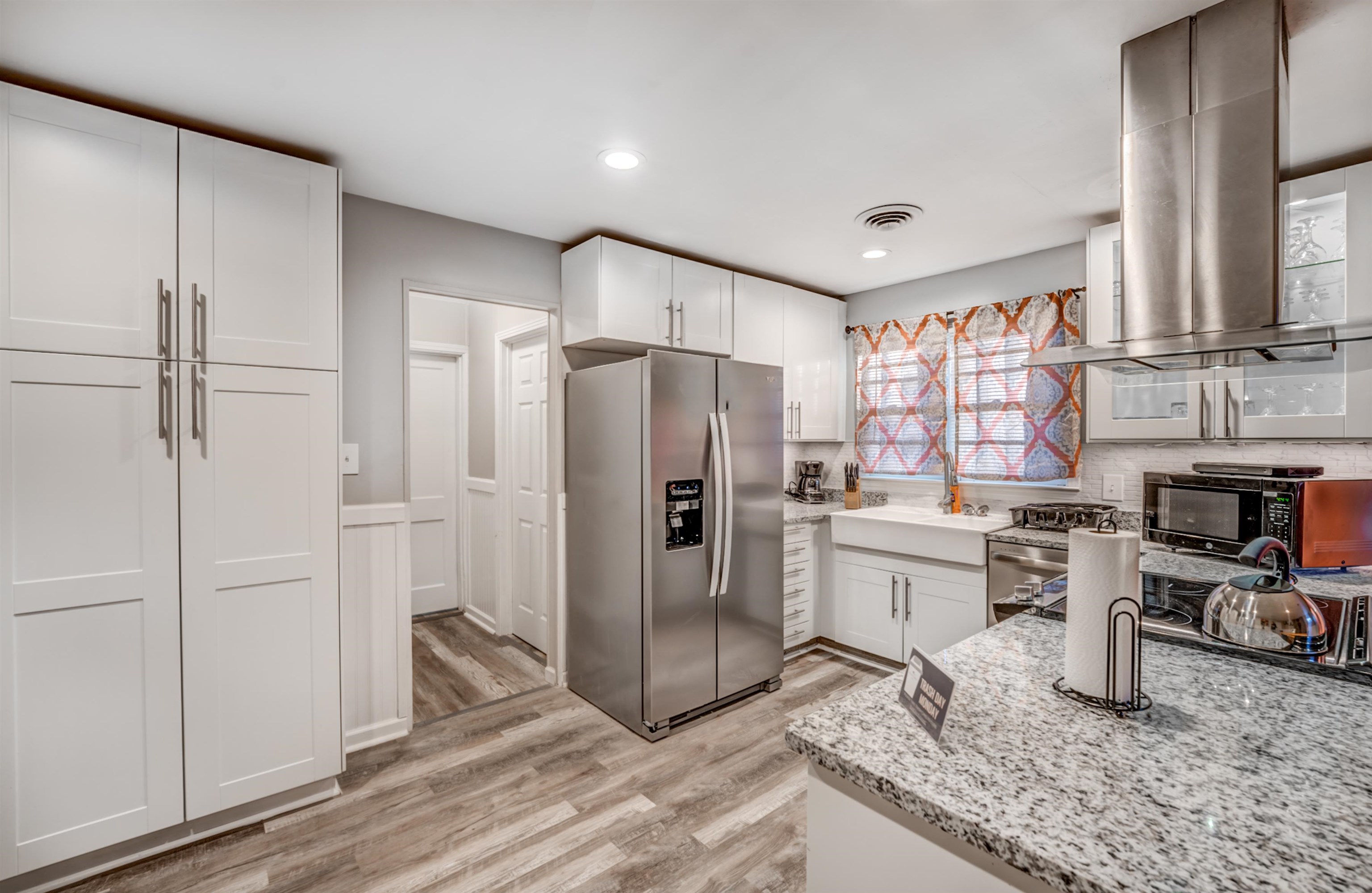 Kitchen with white cabinets, light wood-type flooring, light stone counters, island exhaust hood, and stainless steel appliances