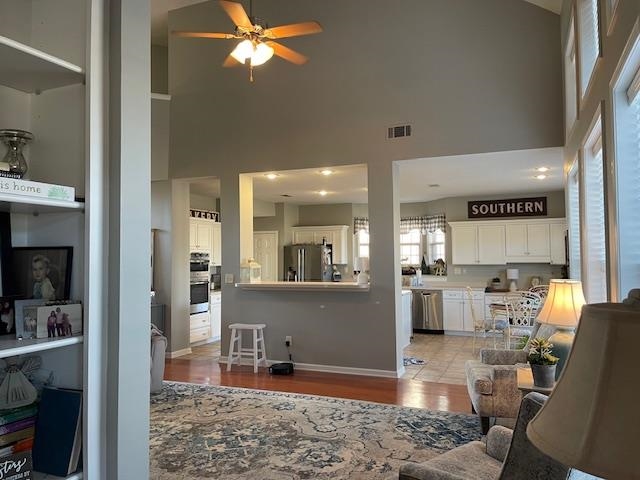 Living room featuring ceiling fan, a towering ceiling, and light hardwood / wood-style flooring