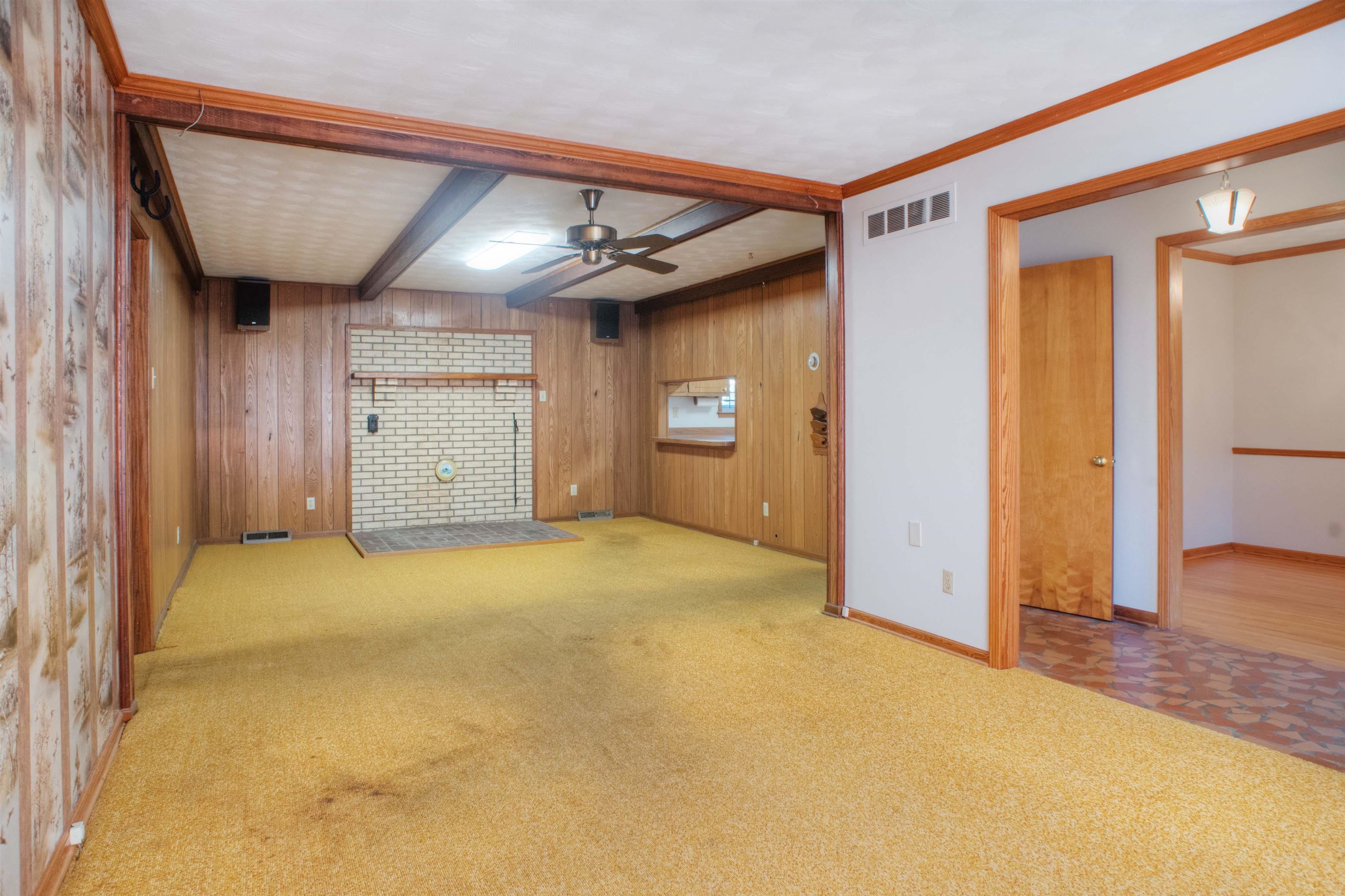 Unfurnished living room featuring beam ceiling, ceiling fan, crown molding, and wood paneled walls