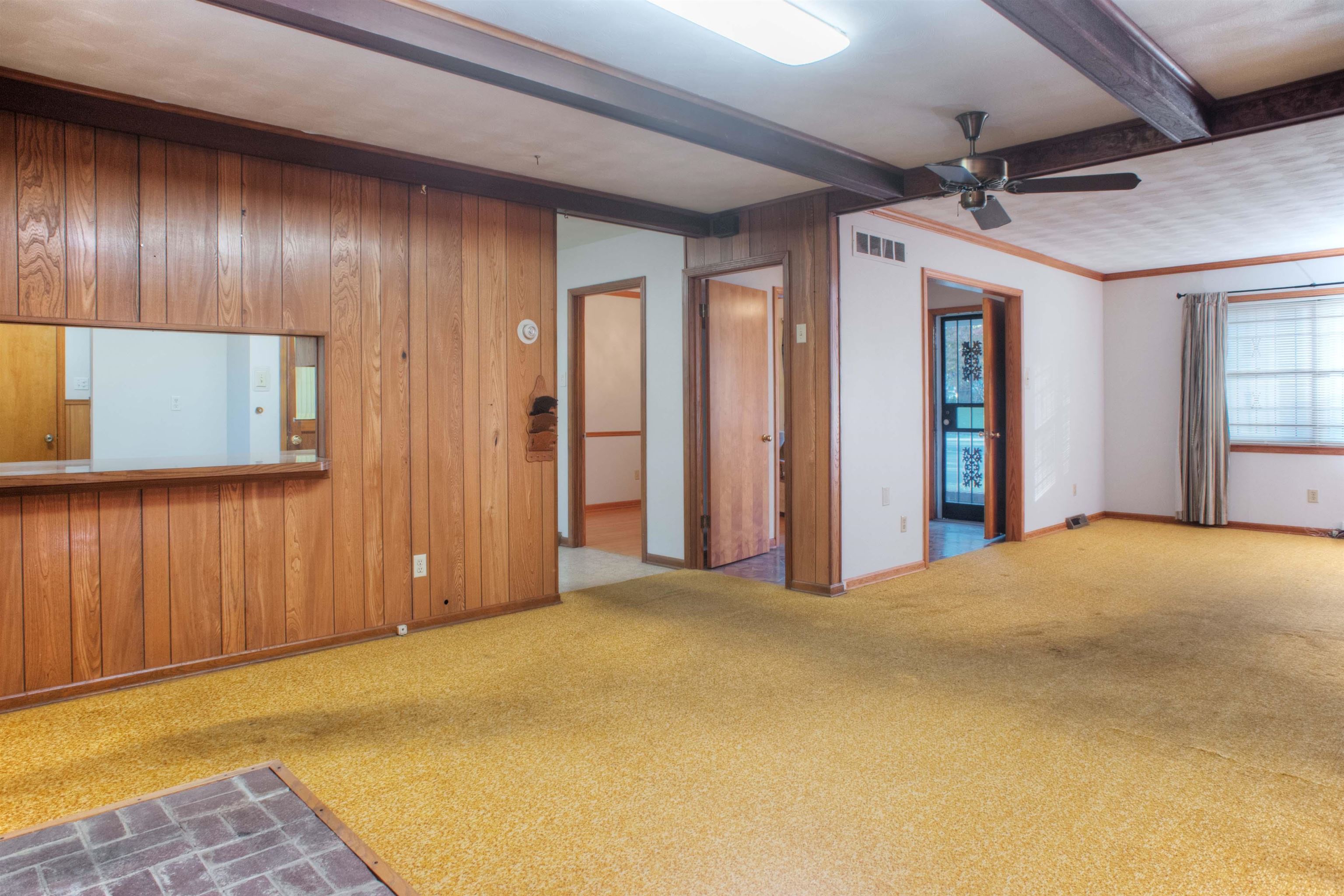 Den and living room featuring wood paneled walls, beamed ceiling, and ornamental molding