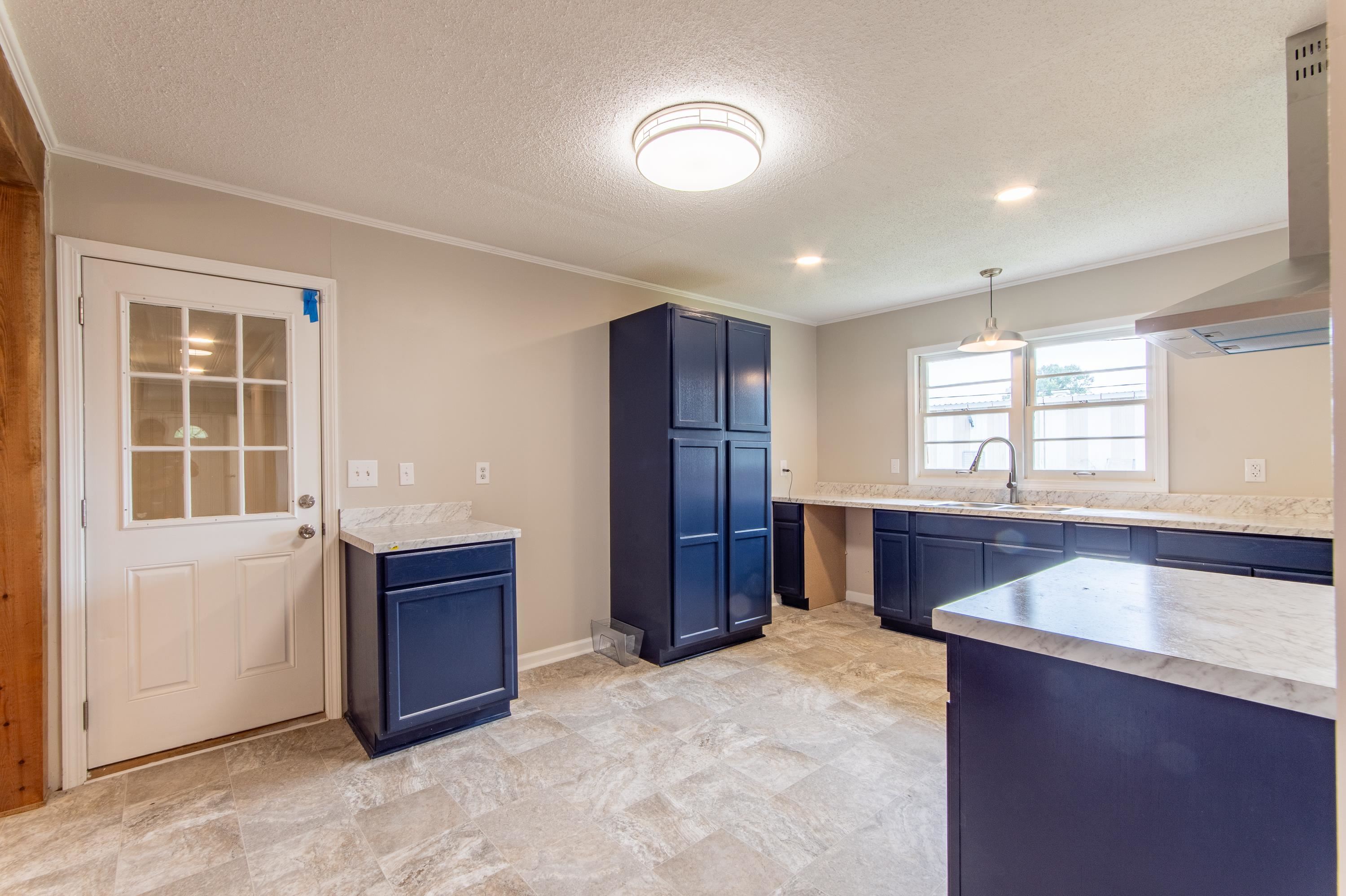 Kitchen featuring wall chimney range hood, sink, a textured ceiling, and light tile patterned floors