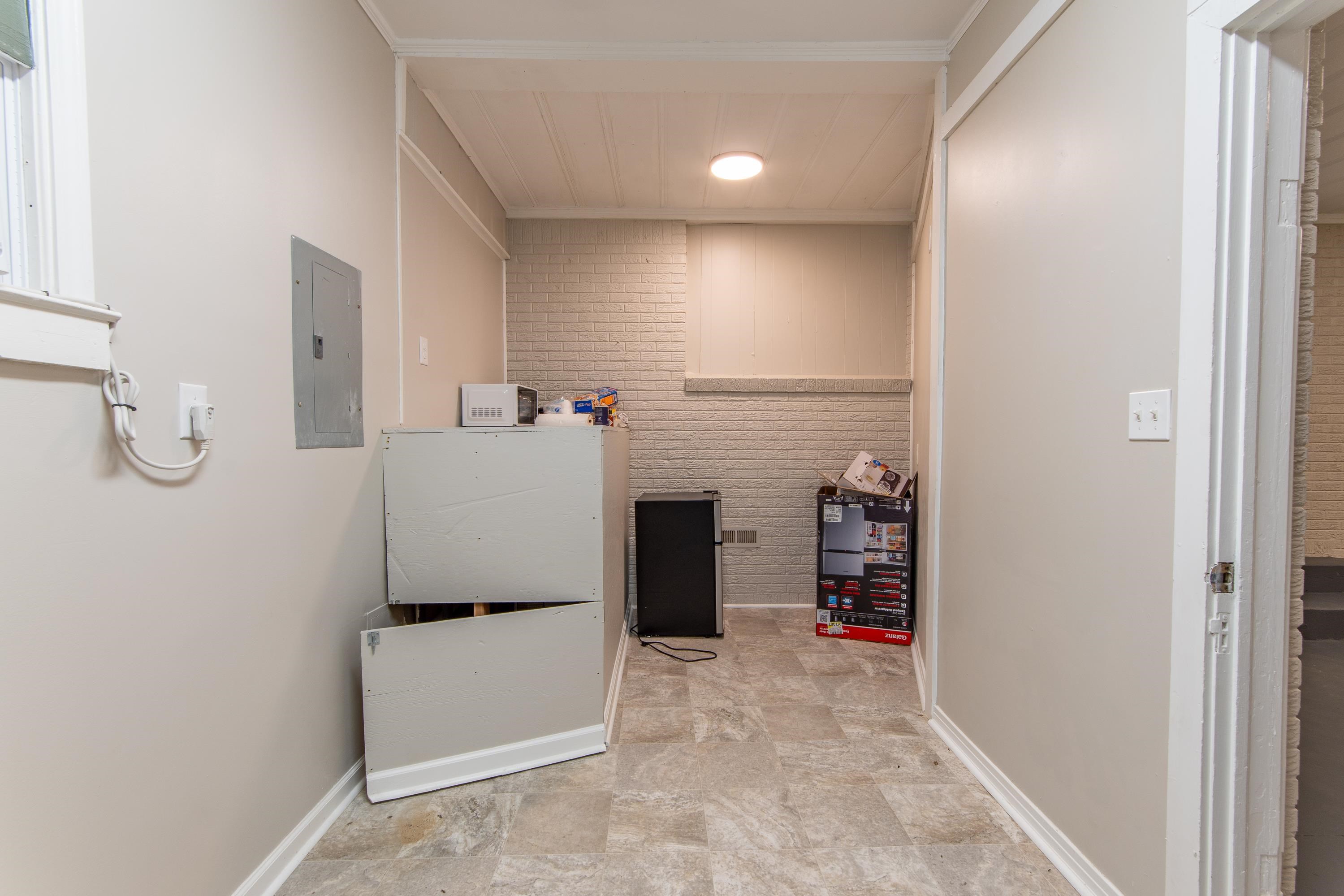 Clothes washing area featuring brick wall, light tile patterned floors, ornamental molding, and electric panel