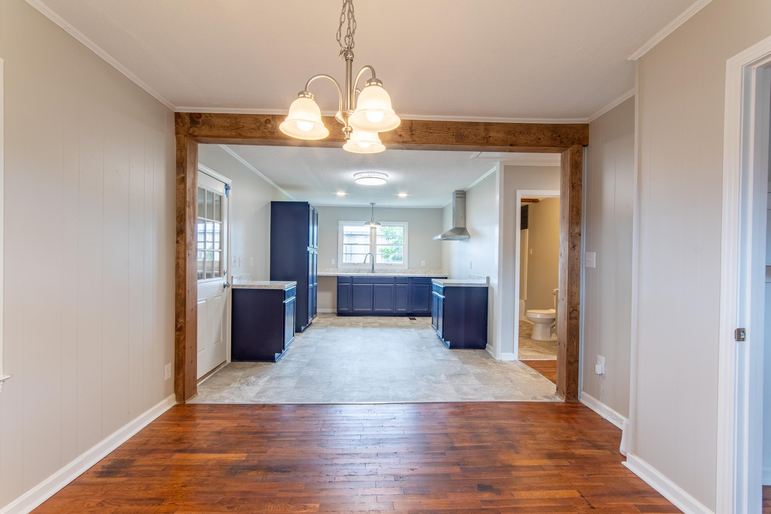 Kitchen with wall chimney range hood, an inviting chandelier, sink, light hardwood / wood-style floors, and blue cabinetry