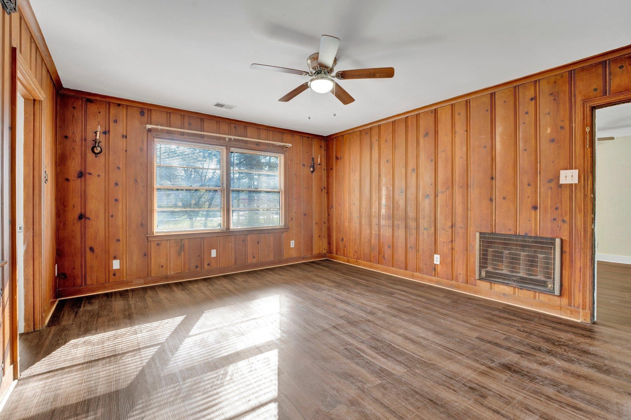 Unfurnished living room with heating unit, ceiling fan, wooden walls, and wood-type flooring