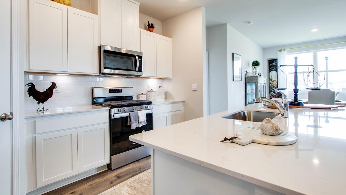 Kitchen featuring appliances with stainless steel finishes, light stone counters, backsplash, light wood-type flooring, and white cabinetry