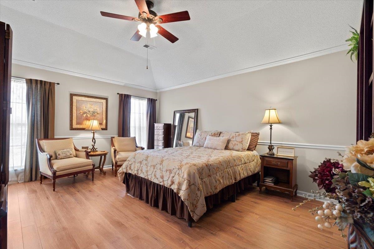 Bedroom with light wood-type flooring, ornamental molding, a textured ceiling, ceiling fan, and lofted ceiling