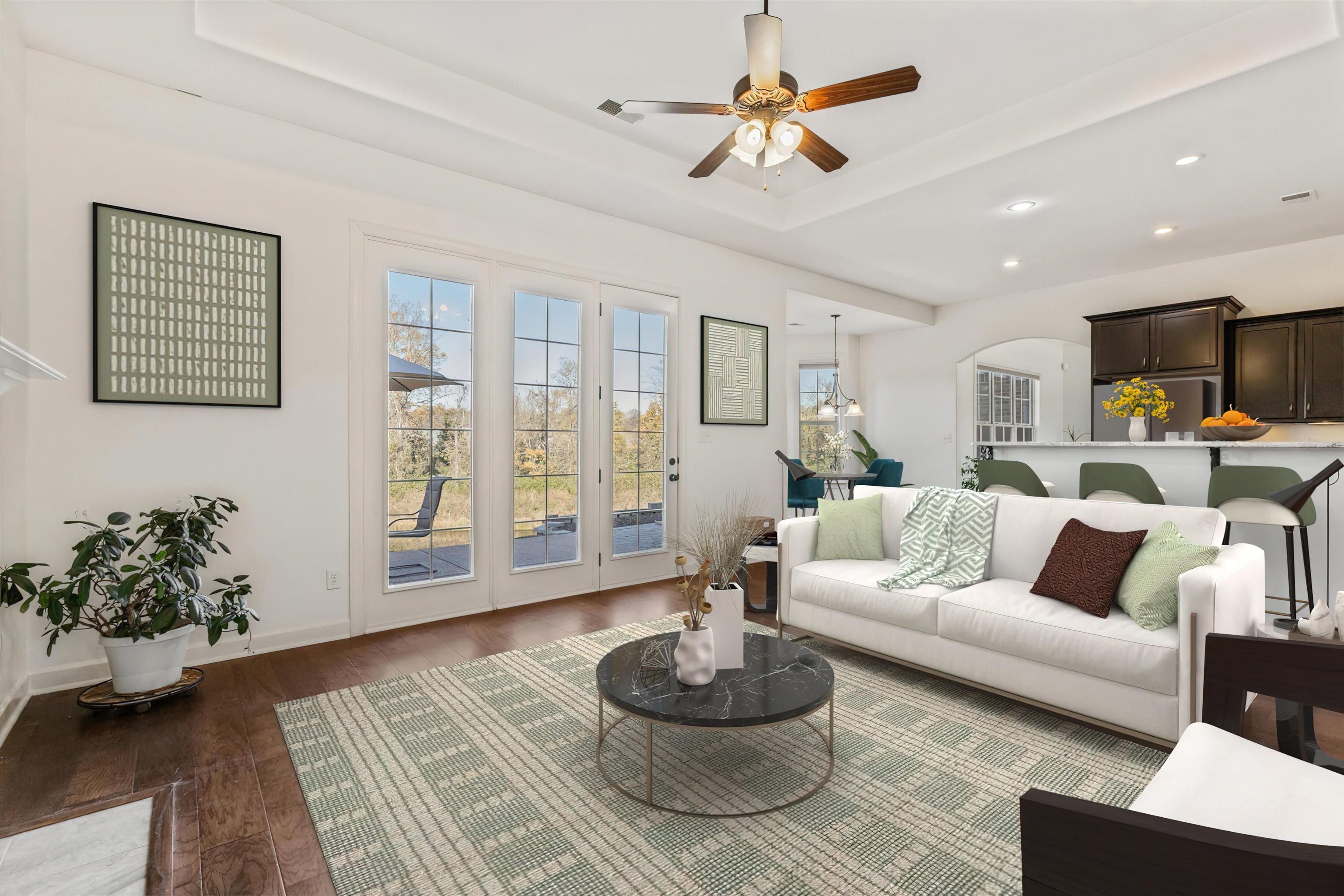 Living room with ceiling fan with notable chandelier, a raised ceiling, and dark wood-type flooring