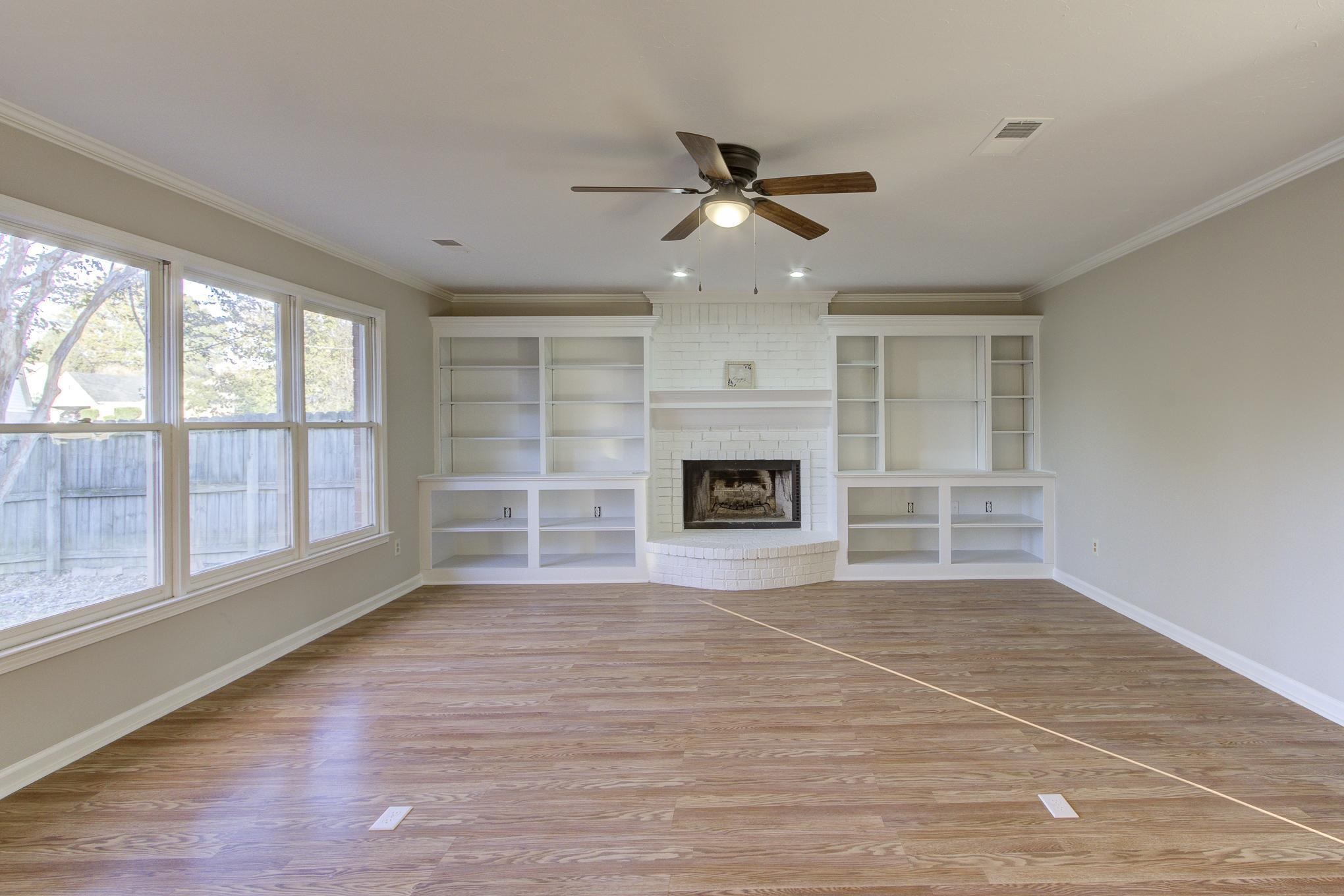 Unfurnished living room featuring light wood-type flooring, a brick fireplace, ceiling fan, and ornamental molding