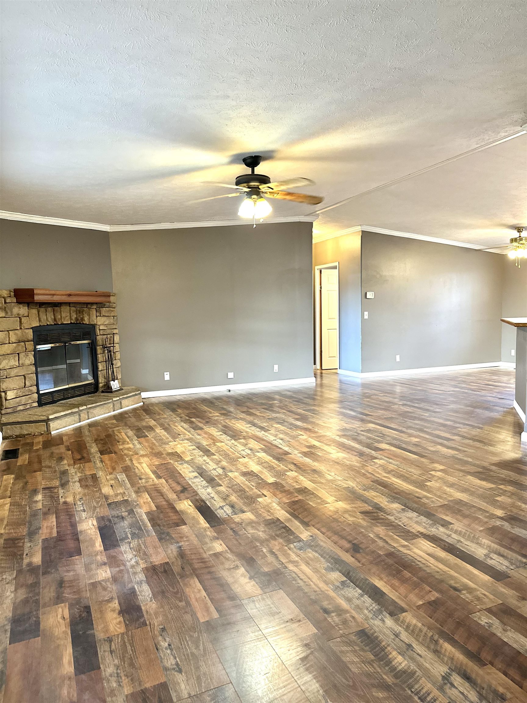 Unfurnished living room featuring ceiling fan, dark hardwood / wood-style floors, crown molding, a textured ceiling, and a fireplace