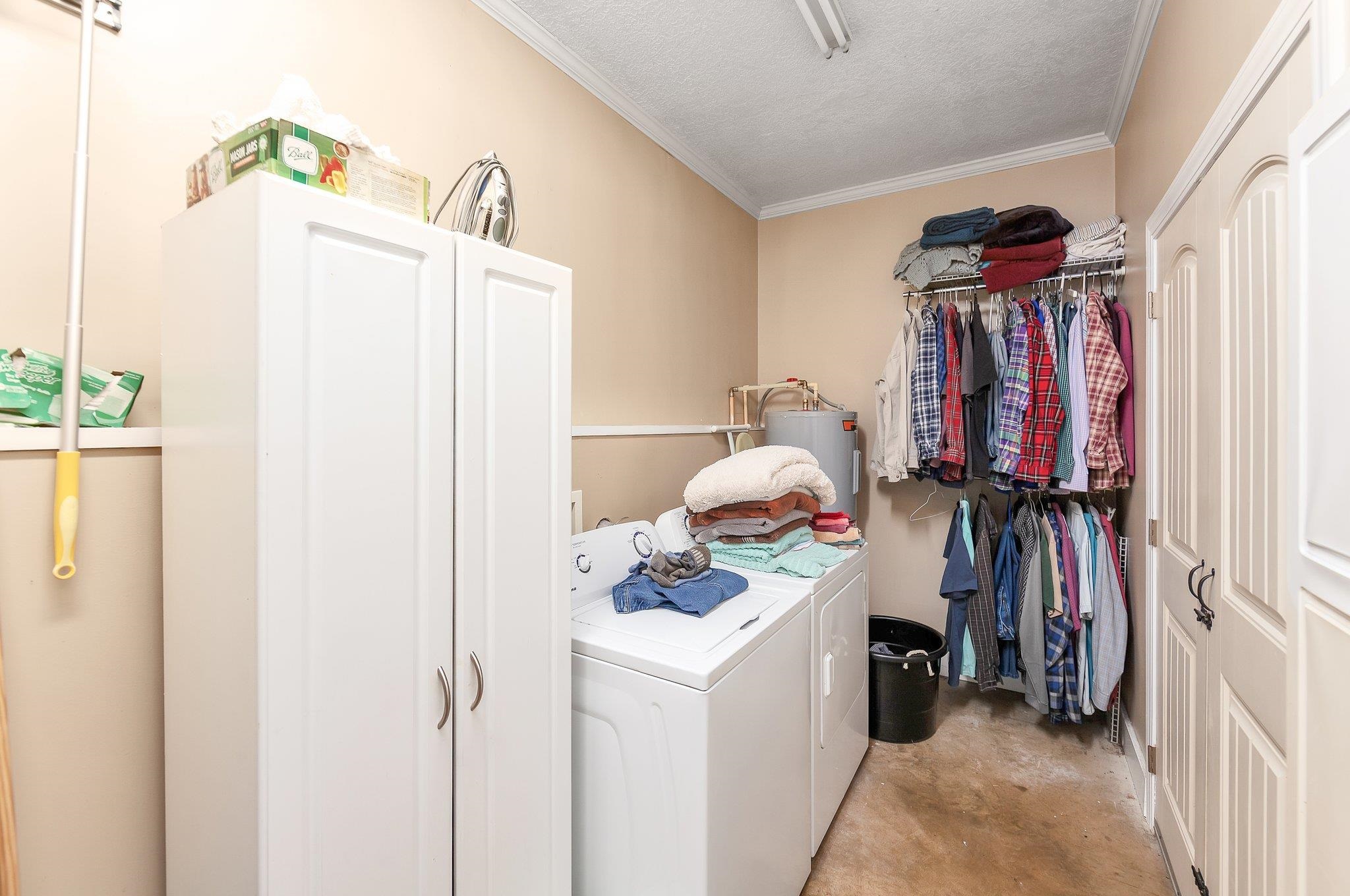 Washroom featuring a textured ceiling, electric water heater, washer and clothes dryer, and ornamental molding