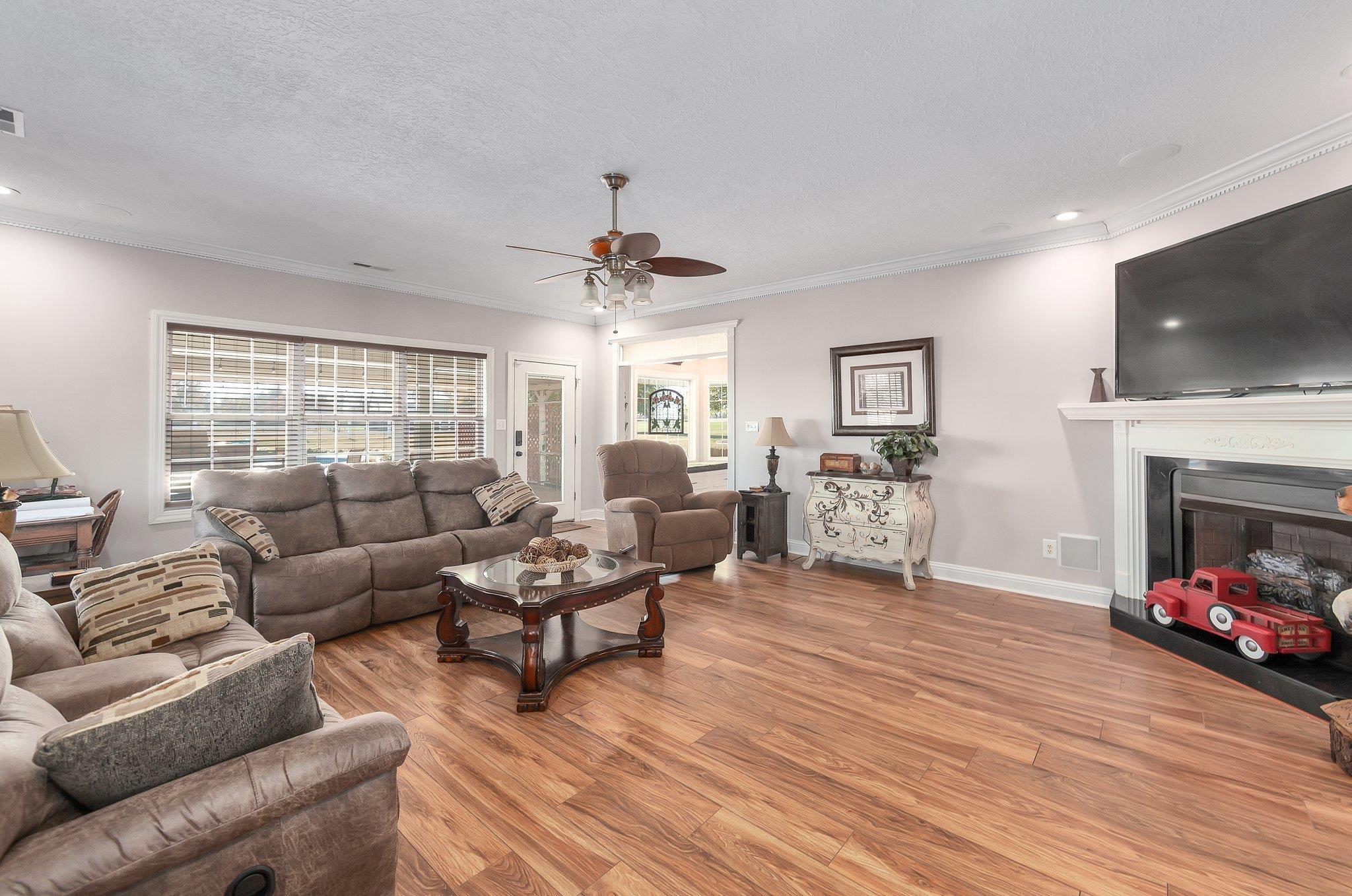 Living room with a textured ceiling, ceiling fan, crown molding, and light hardwood / wood-style flooring