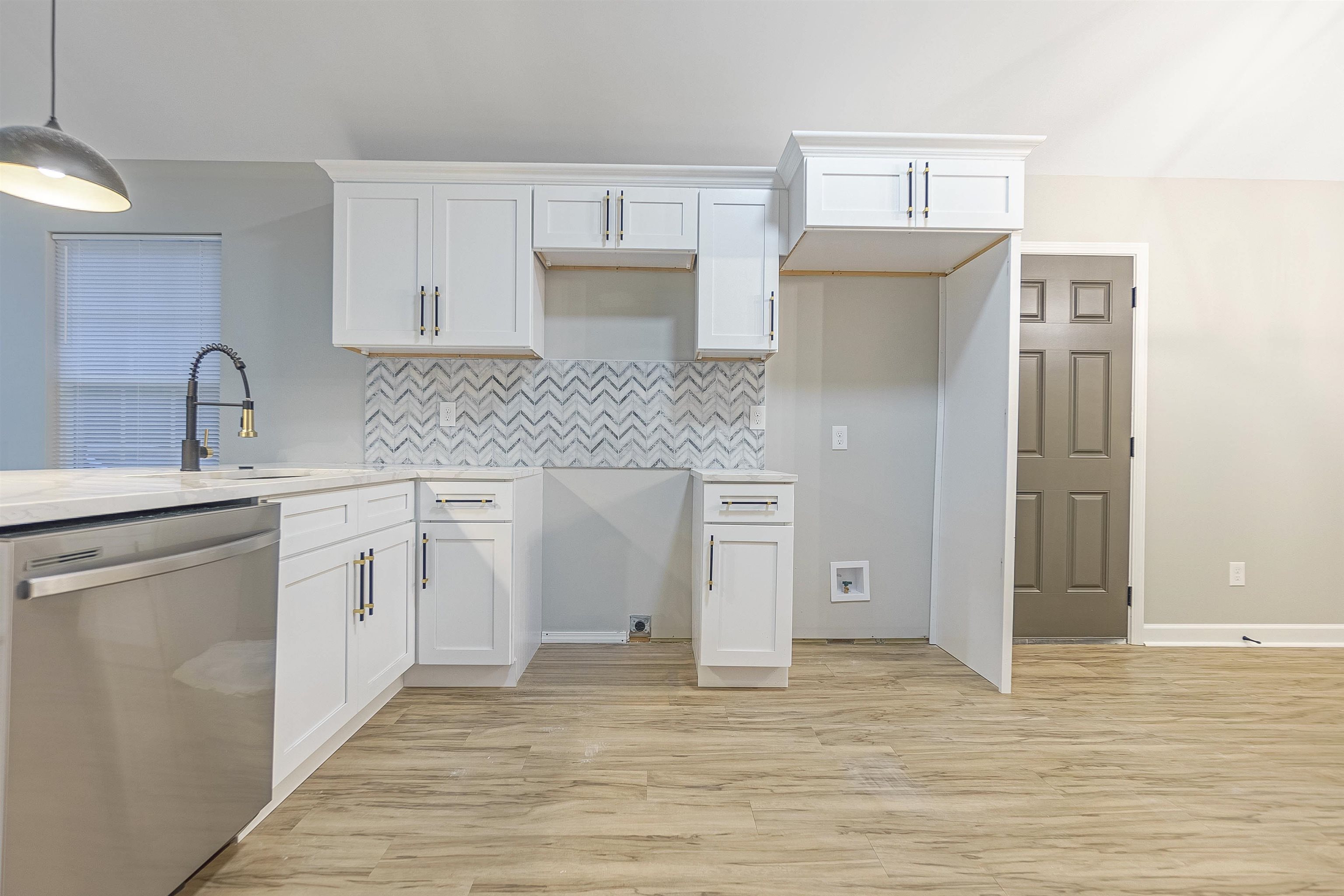 Kitchen with hanging light fixtures, white cabinets, and stainless steel dishwasher