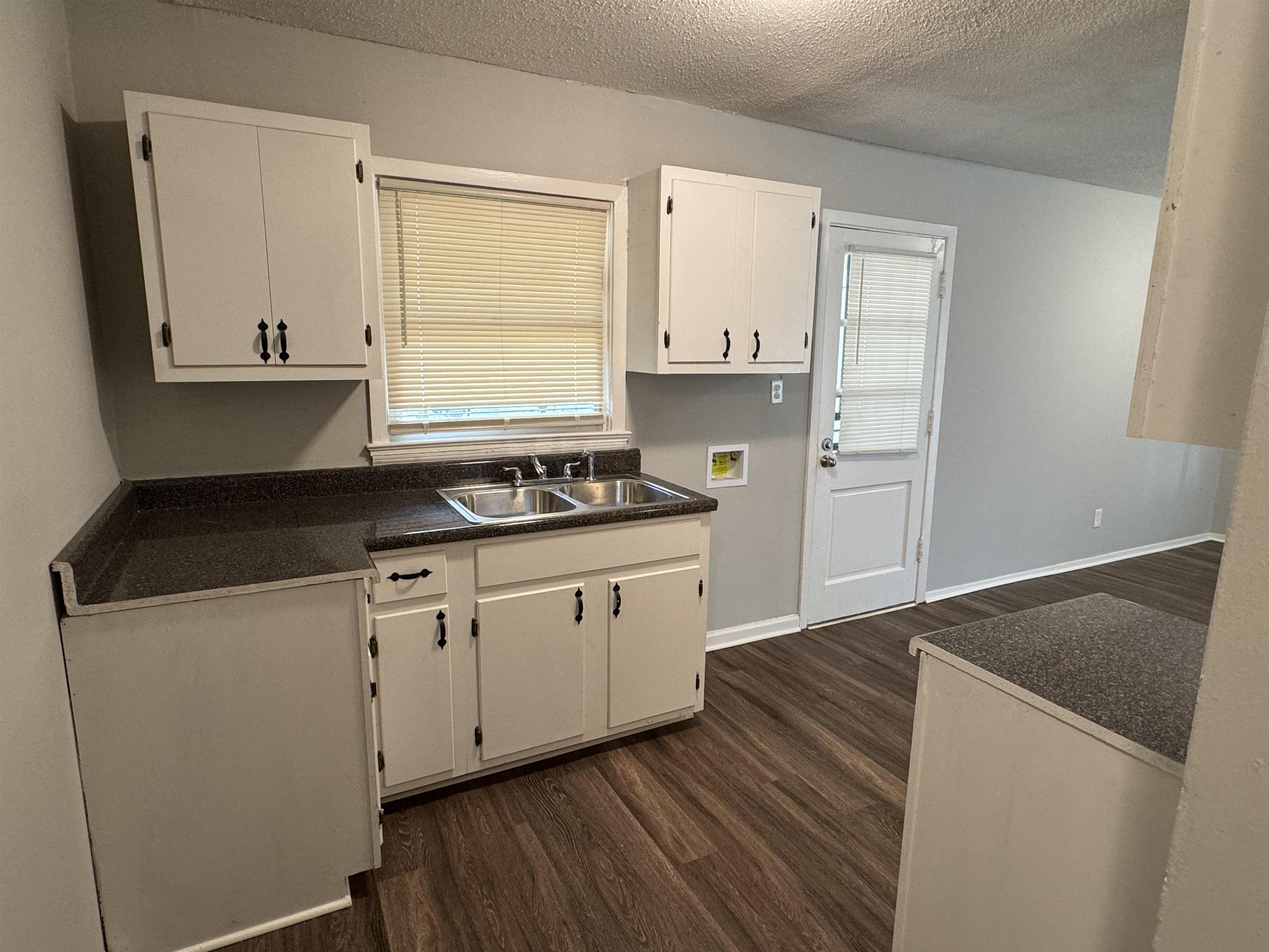 Kitchen featuring a textured ceiling, dark hardwood / wood-style floors, white cabinetry, and sink