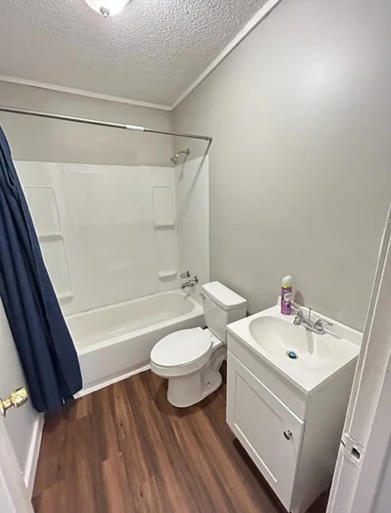 Full bathroom with wood-type flooring, a textured ceiling, toilet, shower / tub combo with curtain, and vanity