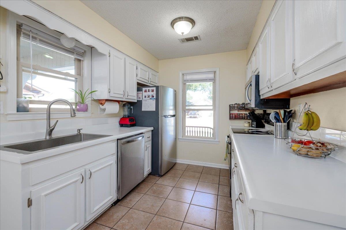 Kitchen with sink, stainless steel appliances, light tile patterned floors, a textured ceiling, and white cabinets