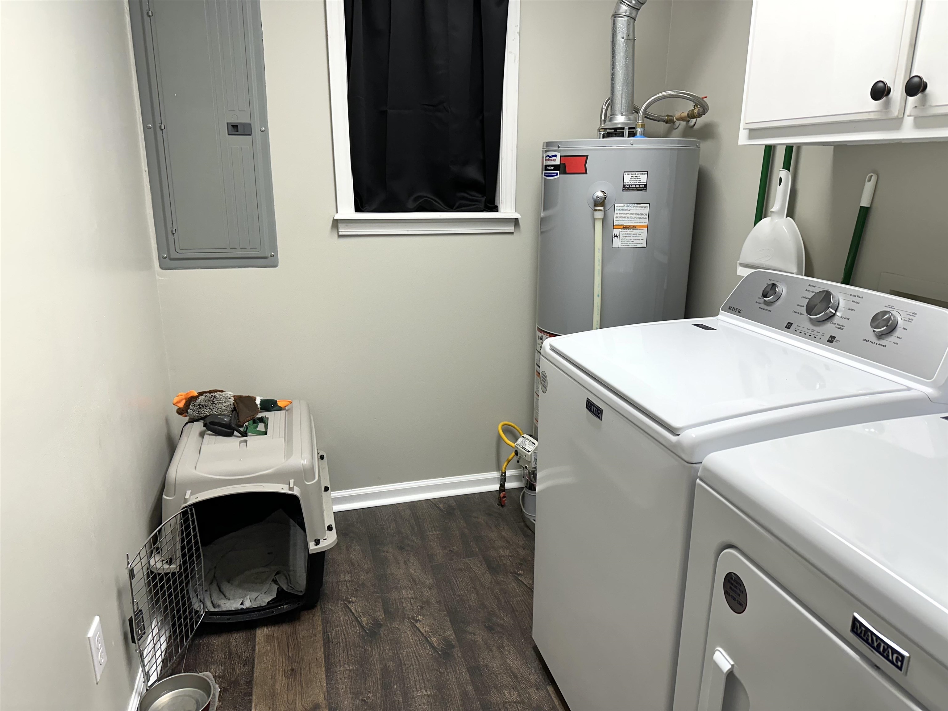 Laundry area with cabinets, gas water heater, dark wood-type flooring, washing machine and dryer, and electric panel