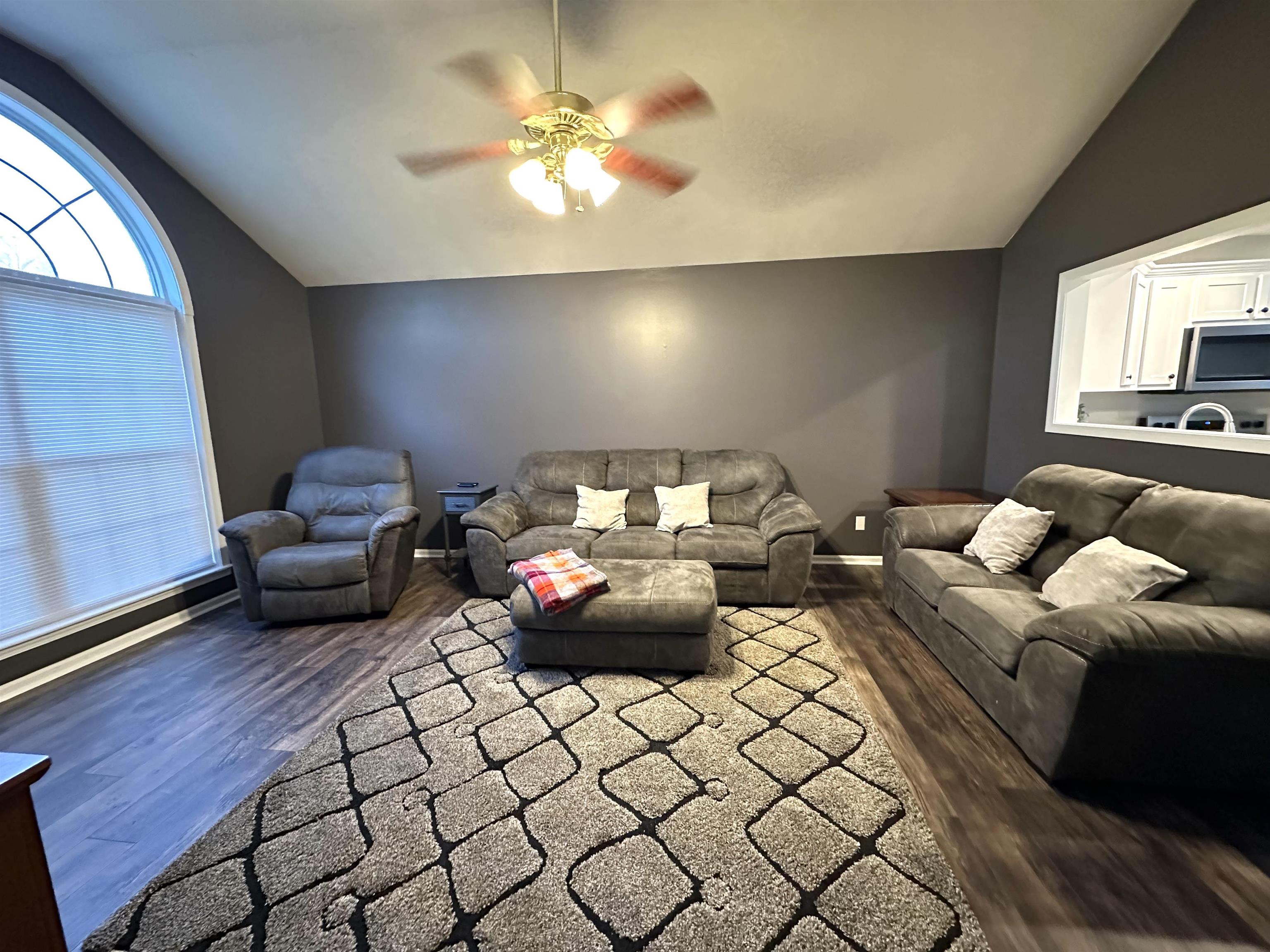 Living room with ceiling fan, dark wood-type flooring, and vaulted ceiling