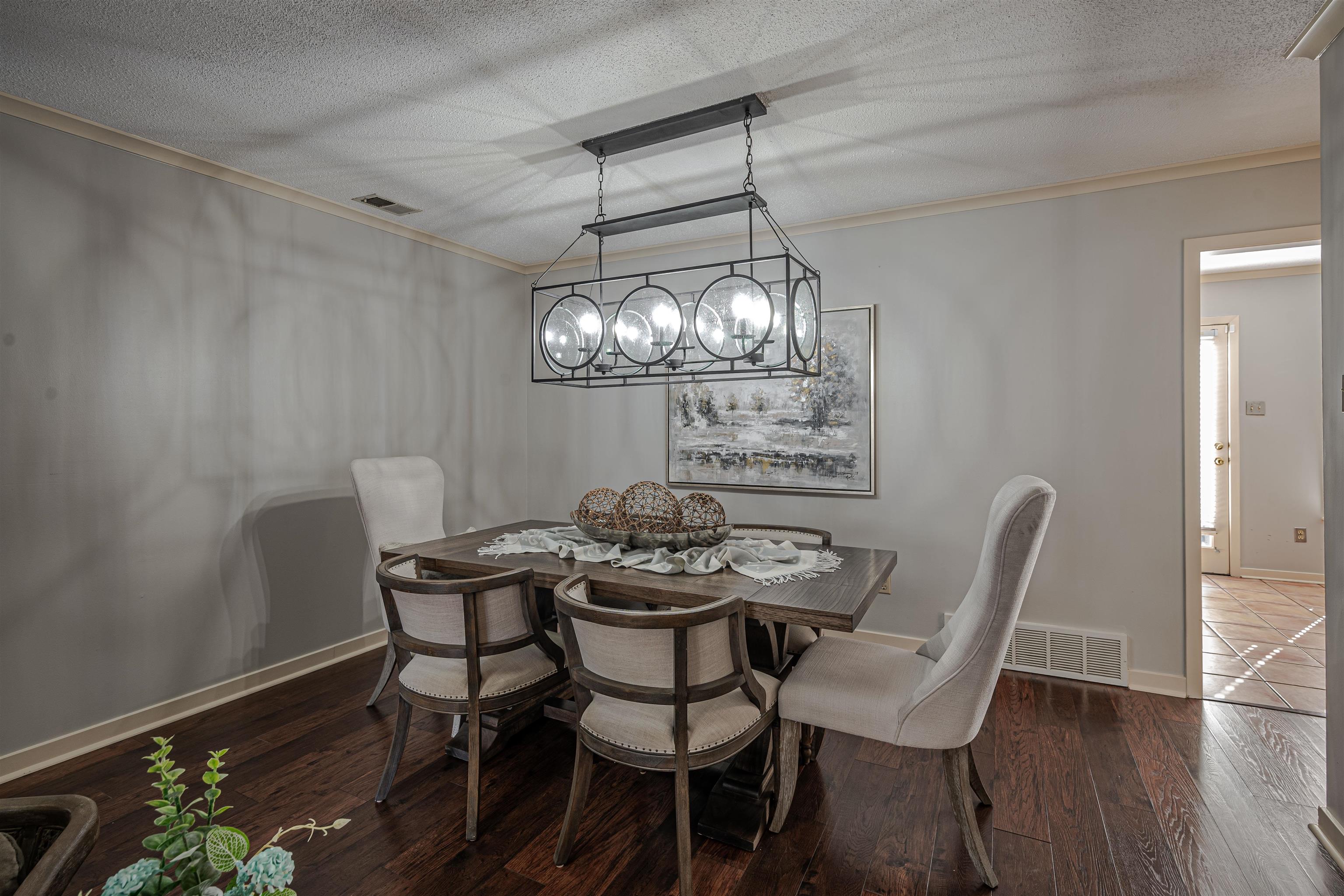 Dining room with a textured ceiling, crown molding, dark wood-type flooring, and a chandelier