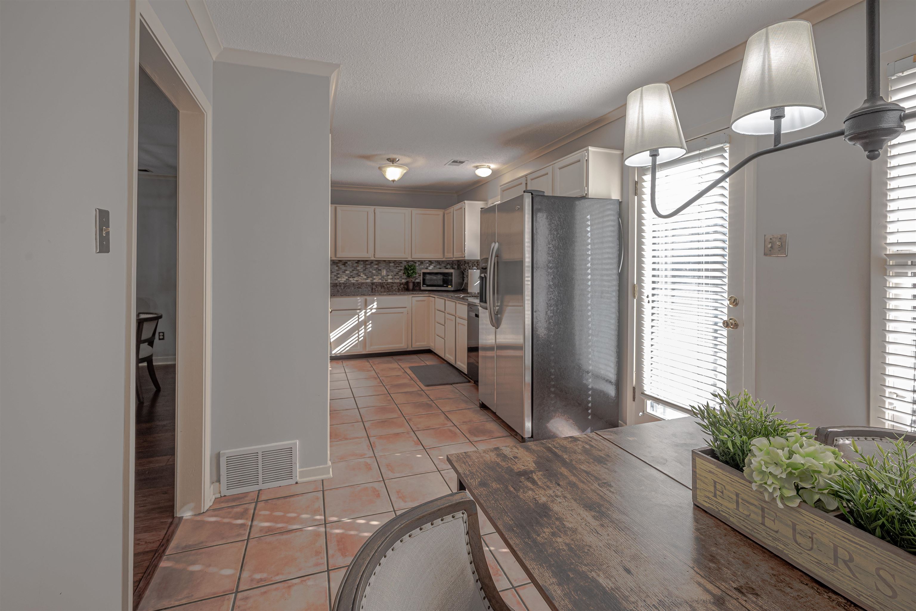 Kitchen featuring decorative backsplash, appliances with stainless steel finishes, a textured ceiling, light tile patterned floors, and white cabinets