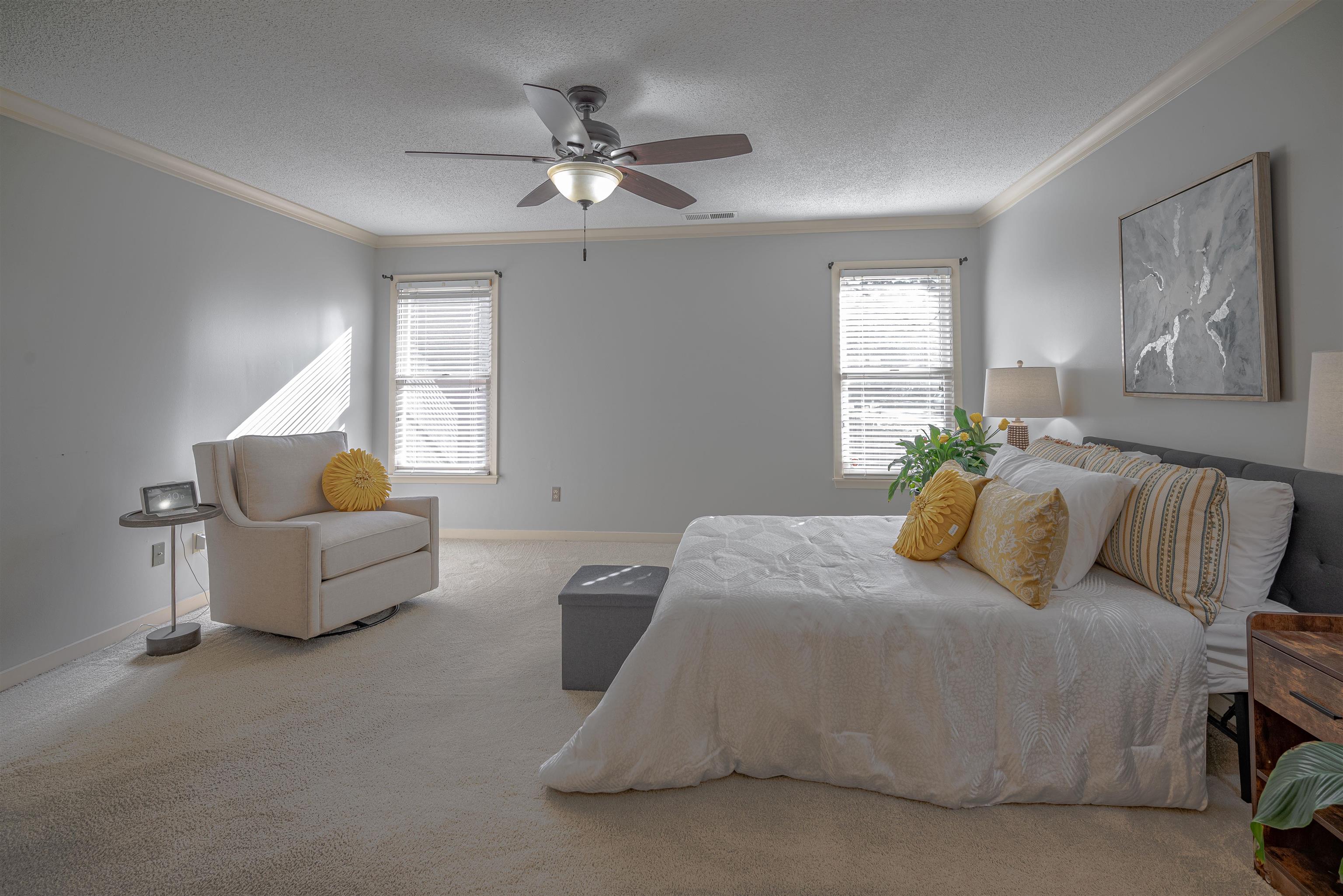 Carpeted bedroom featuring ceiling fan, ornamental molding, and a textured ceiling