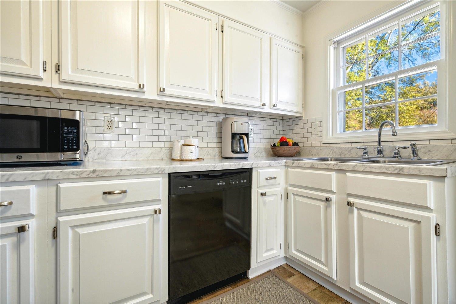 Kitchen with sink, light hardwood / wood-style flooring, black dishwasher, tasteful backsplash, and white cabinetry