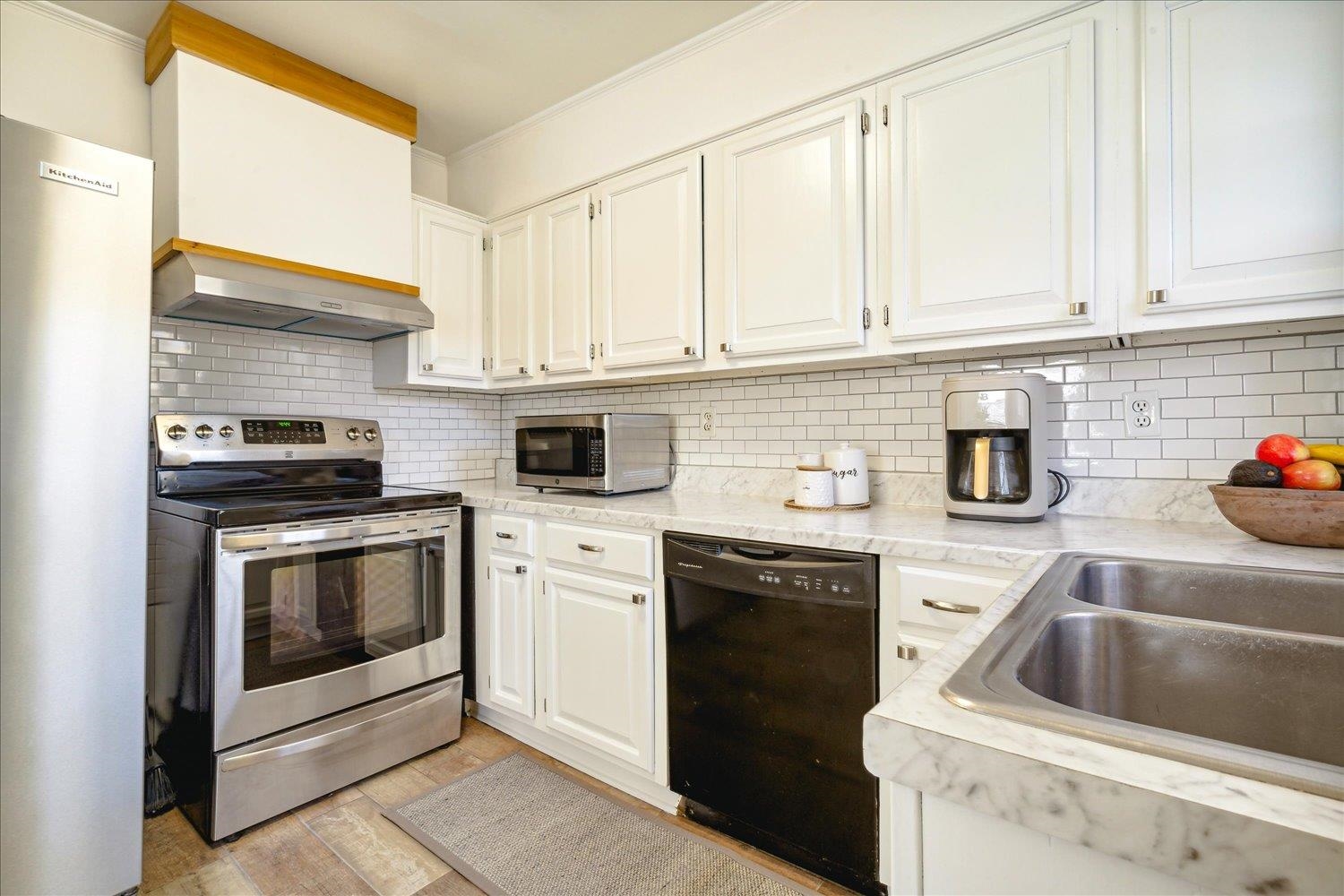 Kitchen featuring white cabinetry, stainless steel appliances, exhaust hood, and tasteful backsplash