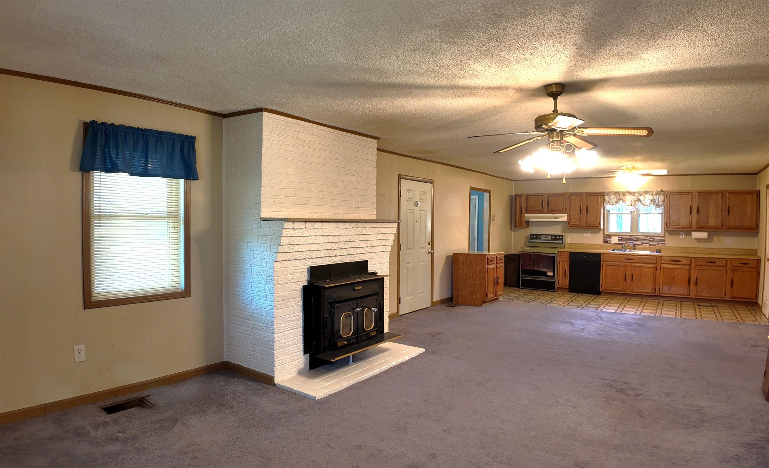 Unfurnished living room featuring a wood stove, a textured ceiling, and light carpet