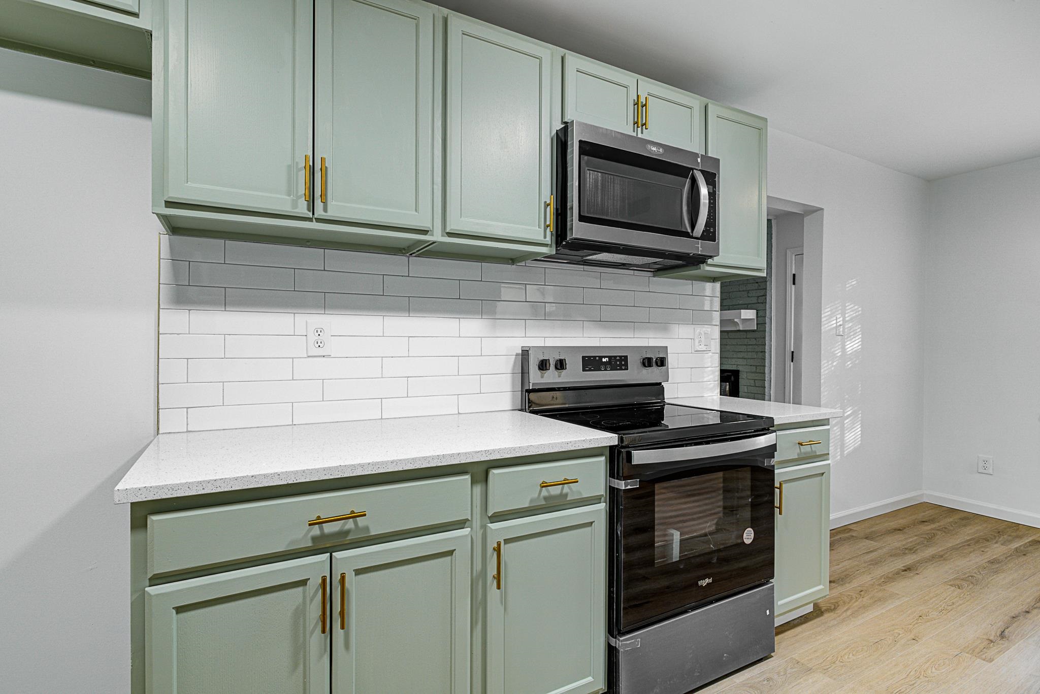 Kitchen with green cabinets, decorative backsplash, stainless steel appliances, and light laminate / wood-style floors